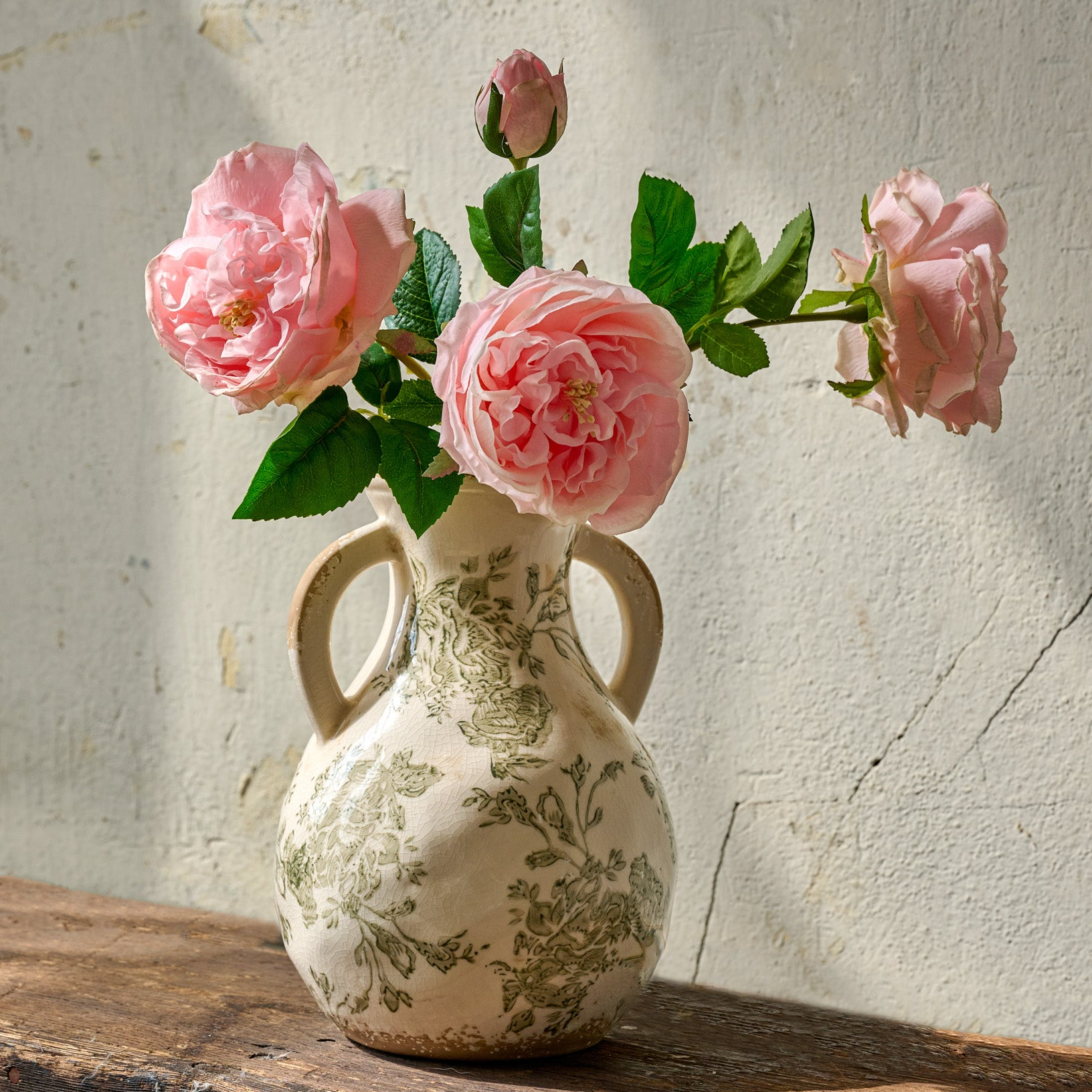 cream and green distressed ceramic vase filled with four pink floral stems.