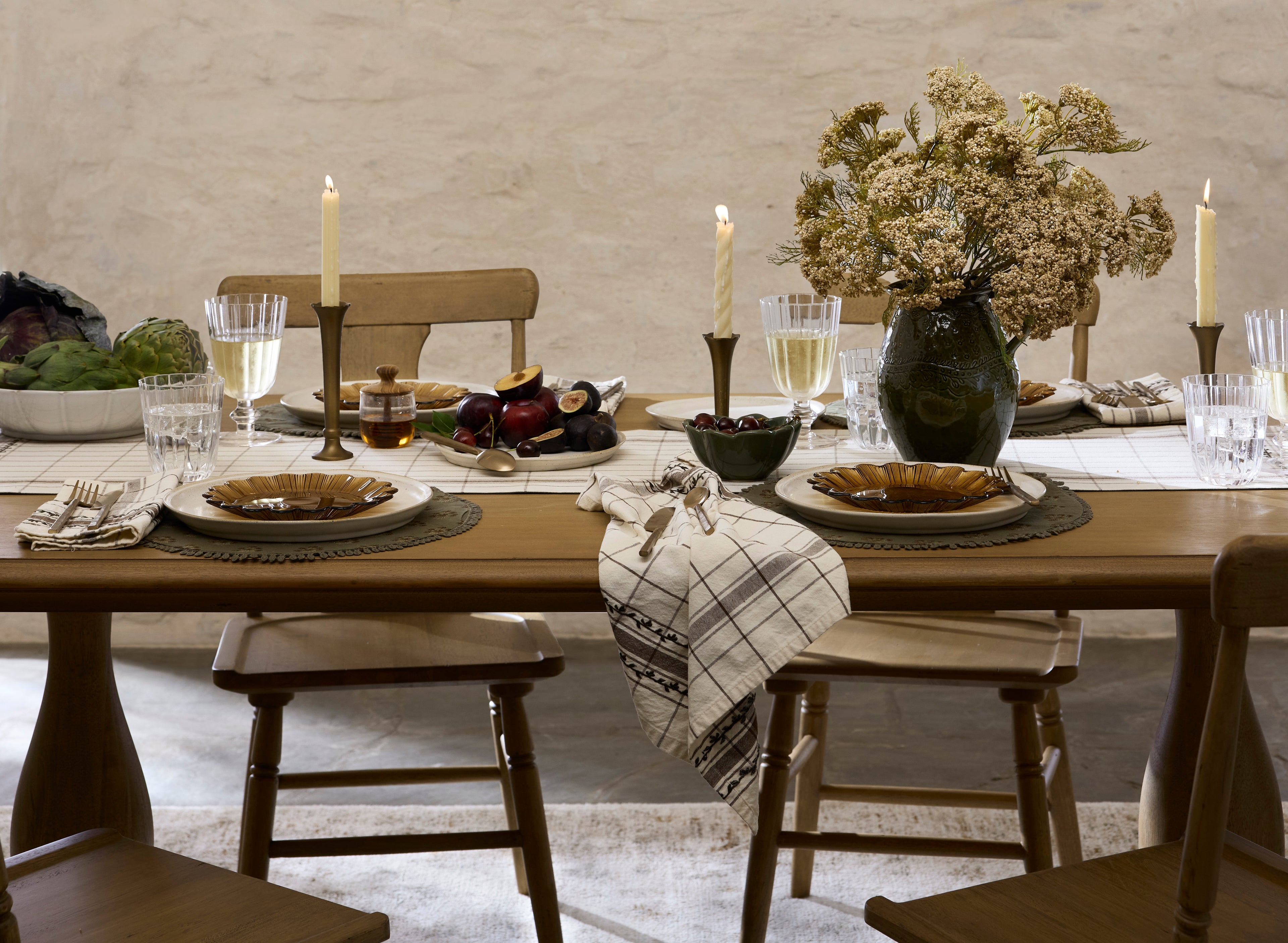 Dining table set with plates, glasses, and candles in a rustic setting.