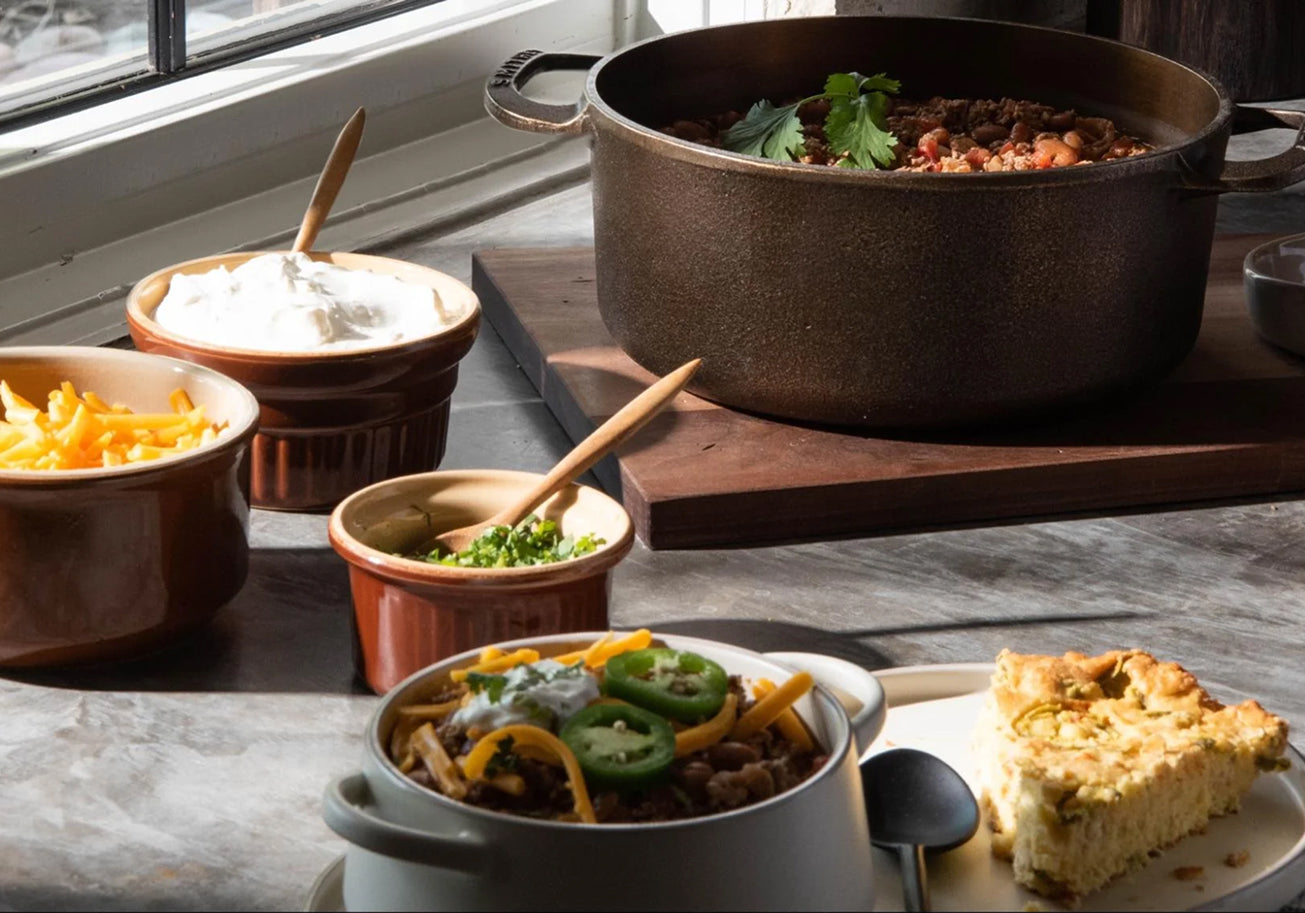 Dish with chili, cornbread, and side dishes on a wooden table.