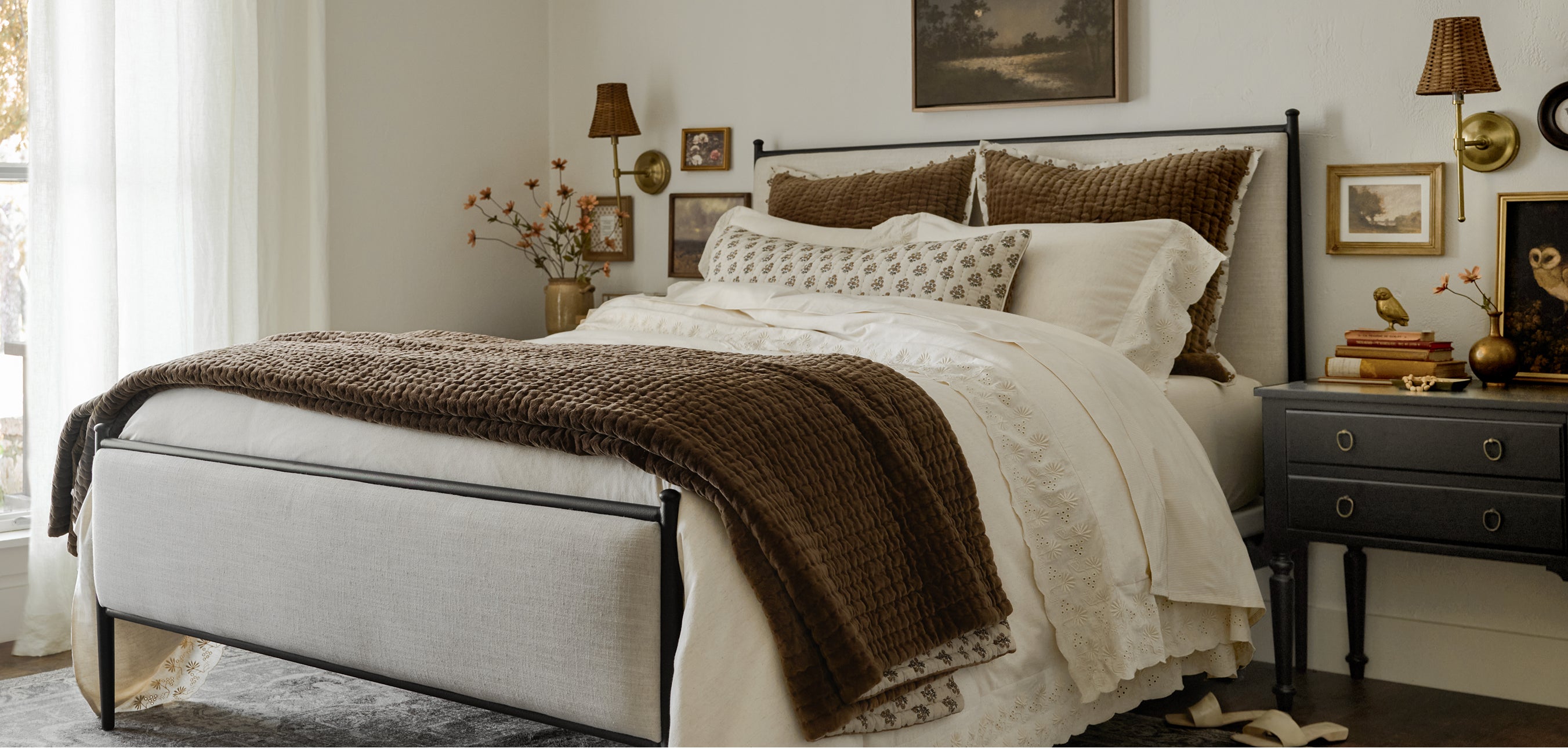 Bedroom with a bed featuring white bedding and brown throw, nightstands with lamps, and framed pictures on the wall.