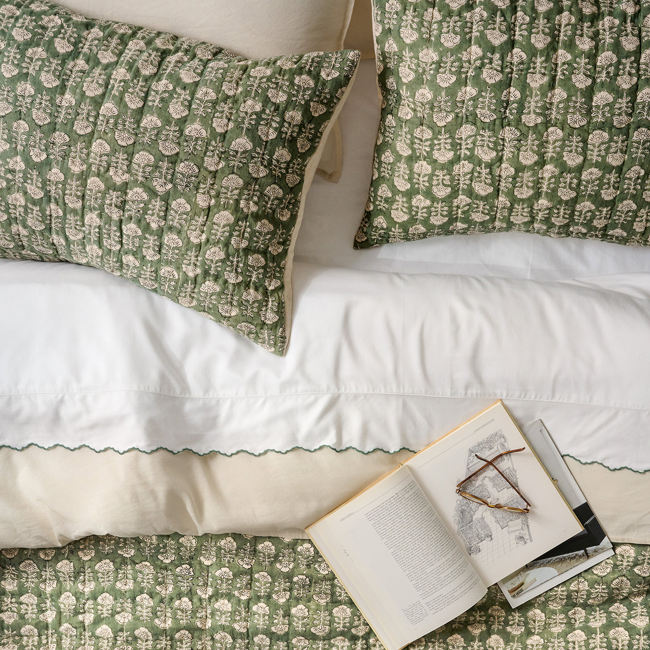 Flora Green patterned pillows and duvet cover on a bed with an open book.