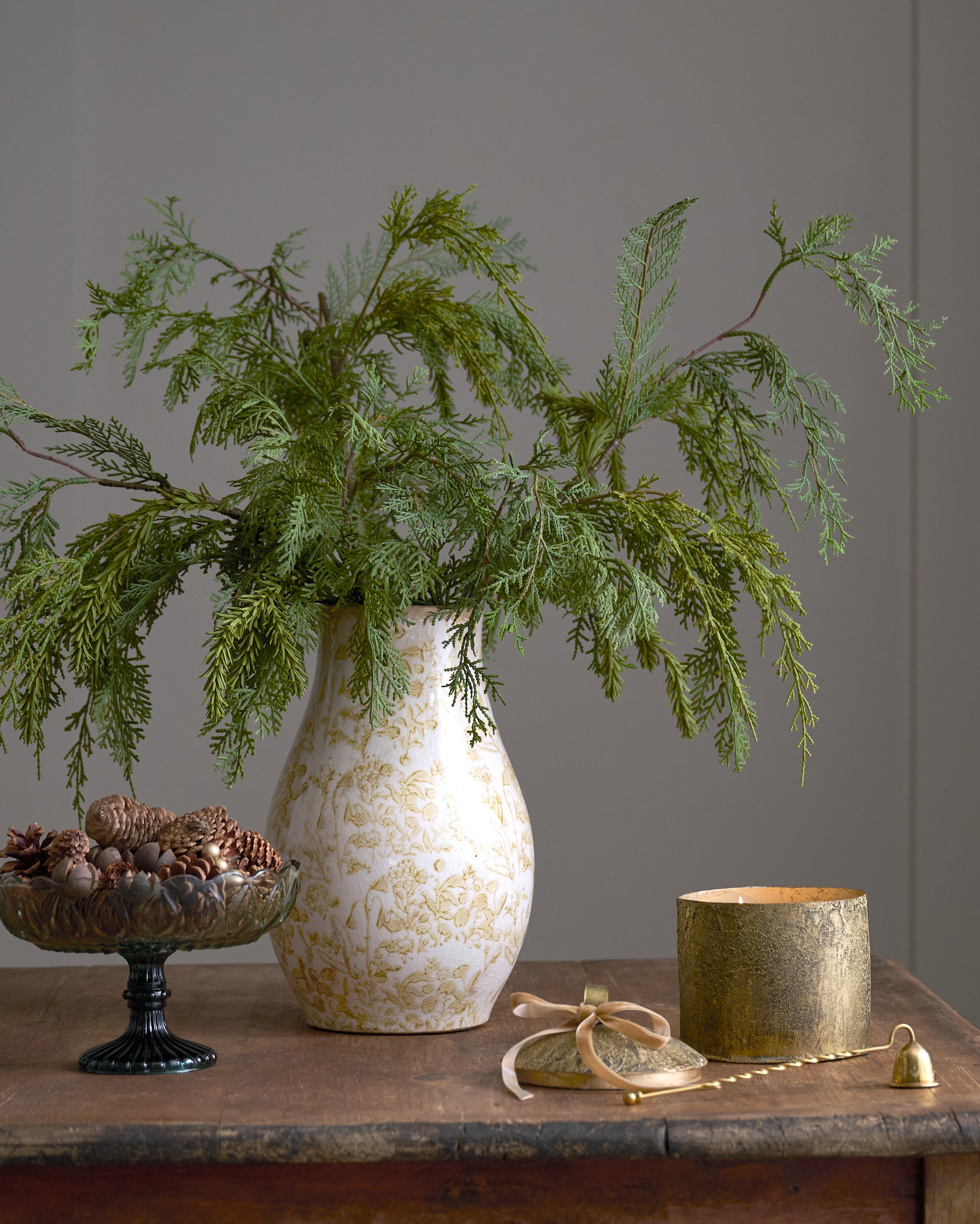 Decorative setting with a vase of greenery, candle, and small bowl on a wooden surface.