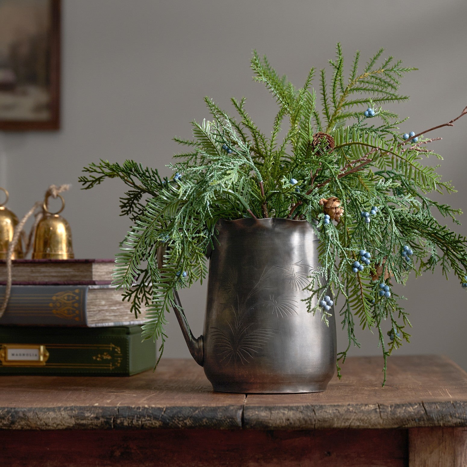 Decorative pitcher with greenery on a wooden surface against a gray wall