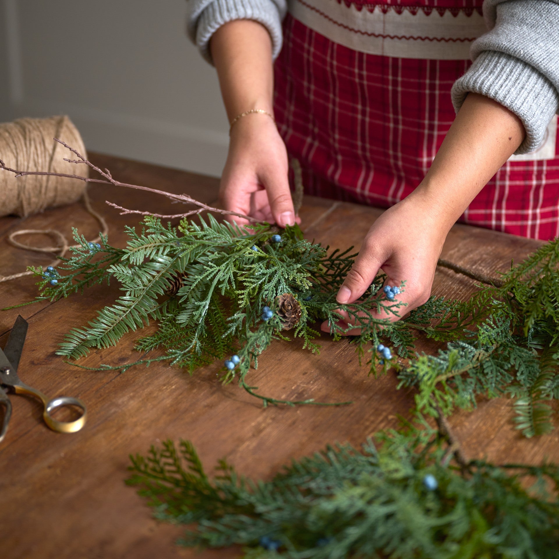 person arranging juniper berry greenery stems on a wooden table