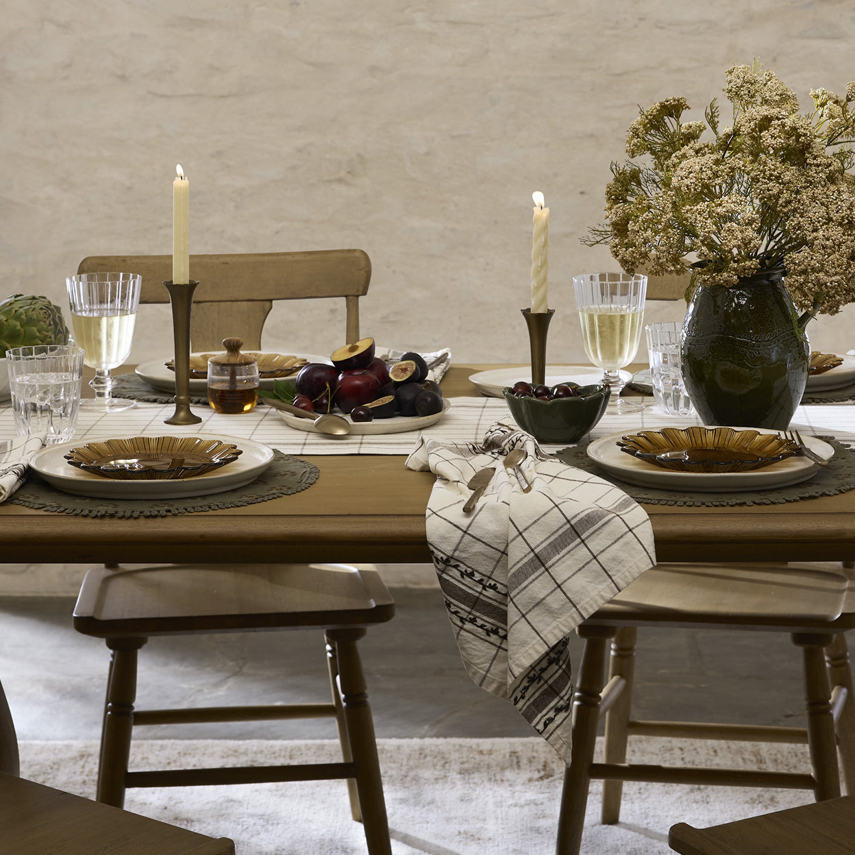 Dining table set with plates, glasses, candles, and a vase with flowers in a rustic setting.