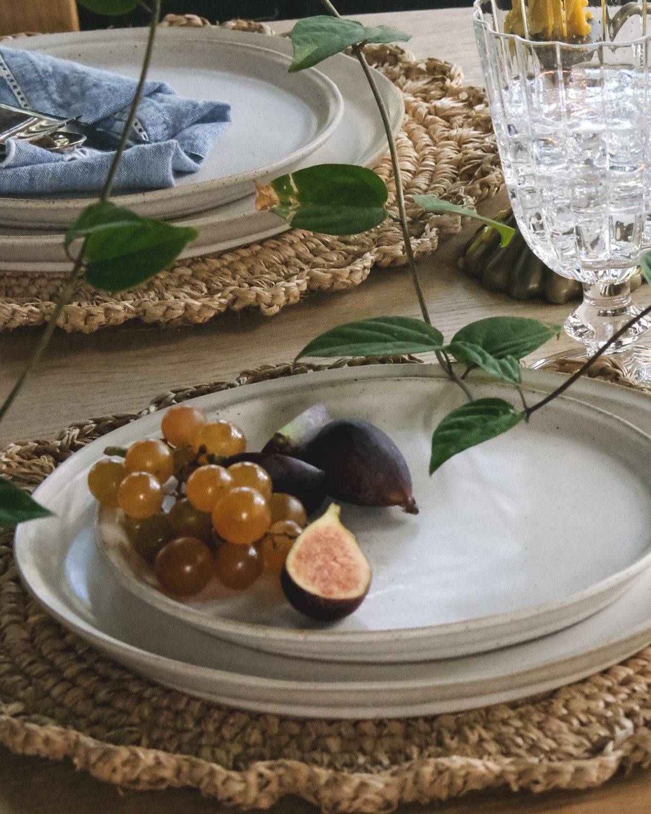 Table setting with white plates, grapes, and figs on a woven placemat.