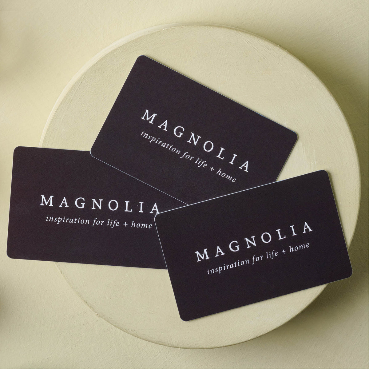 Three black rectangular Magnolia cards with white text, arranged on a round beige surface.