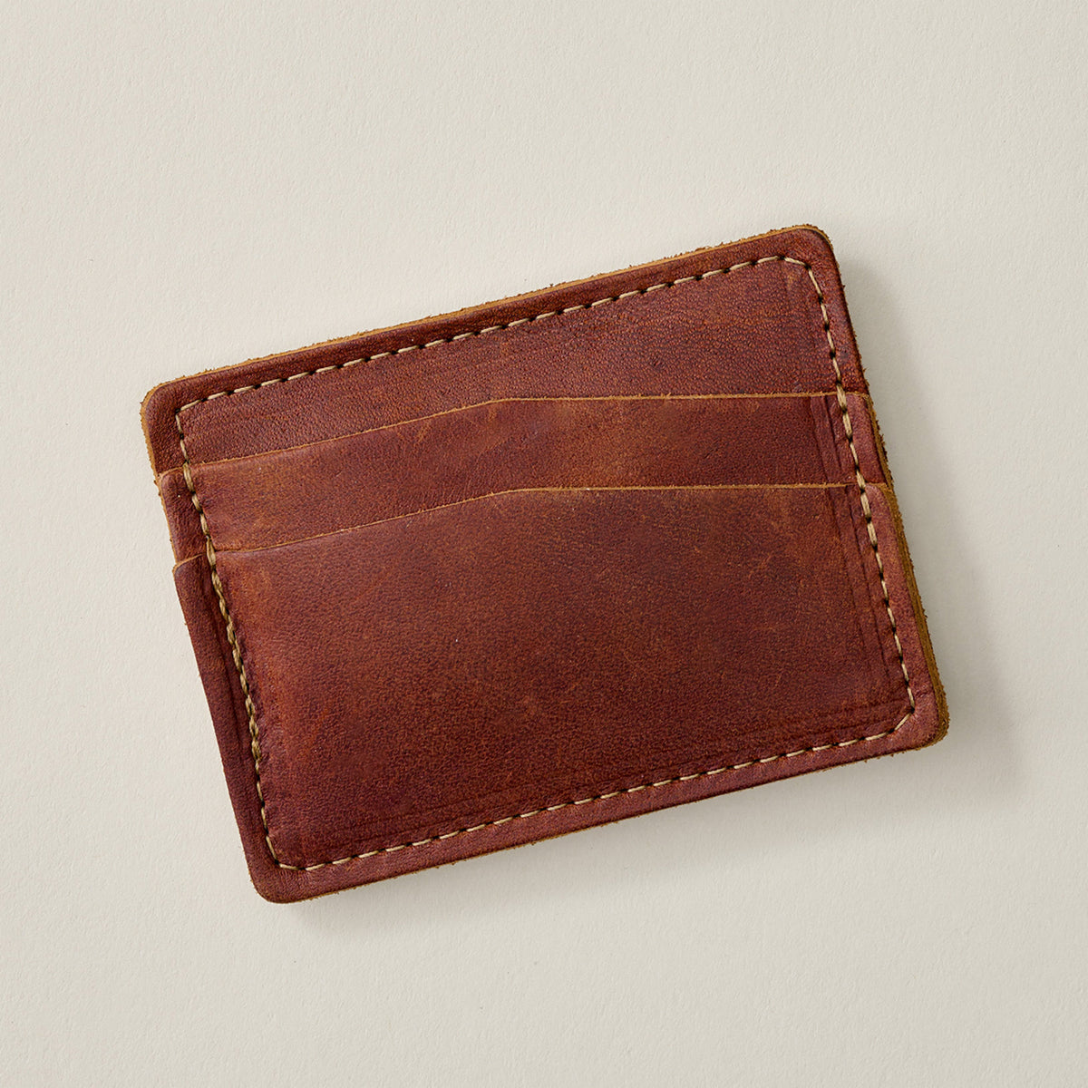 A slim brown leather card holder wallet with visible stitching and card slots, photographed on a plain light beige background.