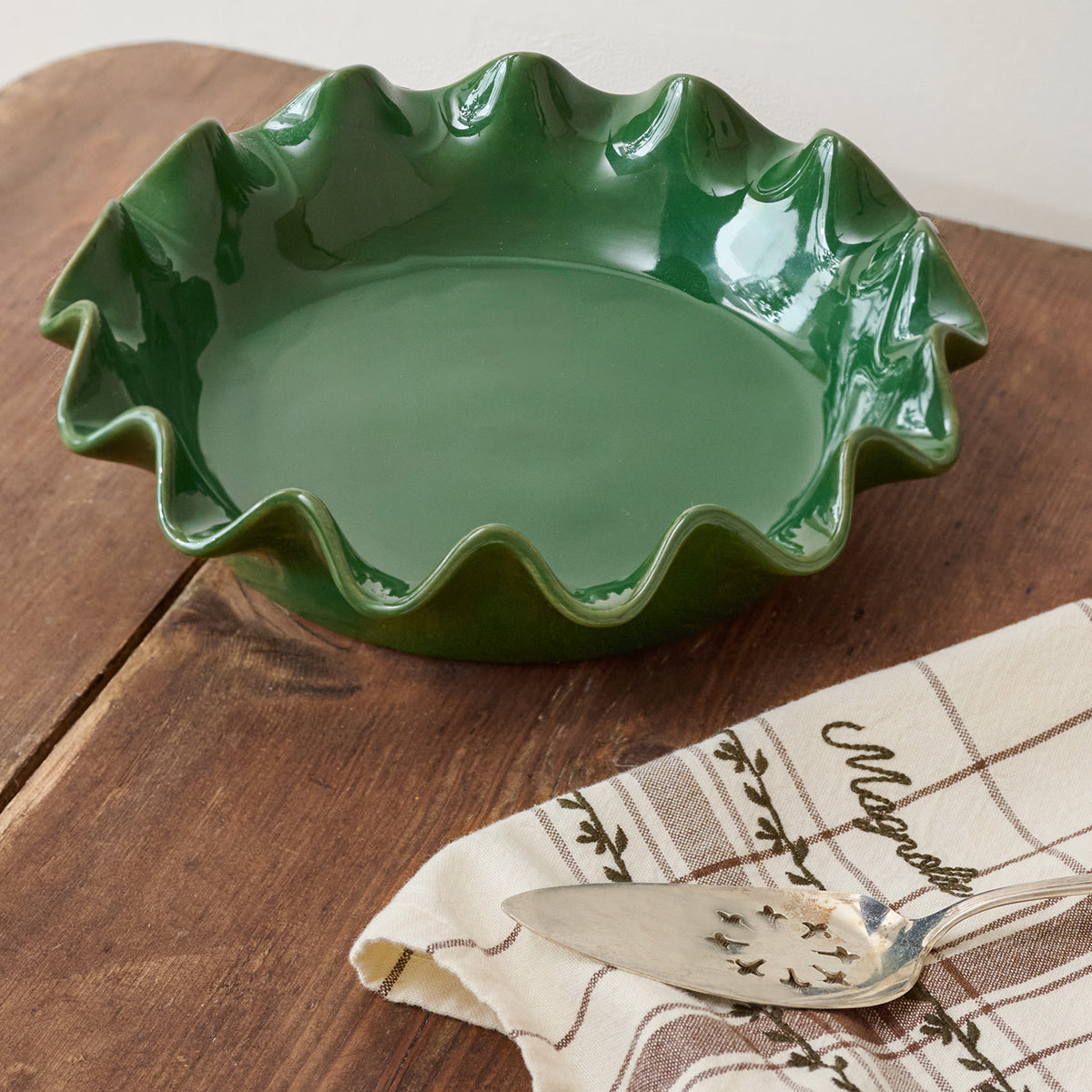 Green ceramic pie dish on a wooden surface with a patterned cloth and spoon.