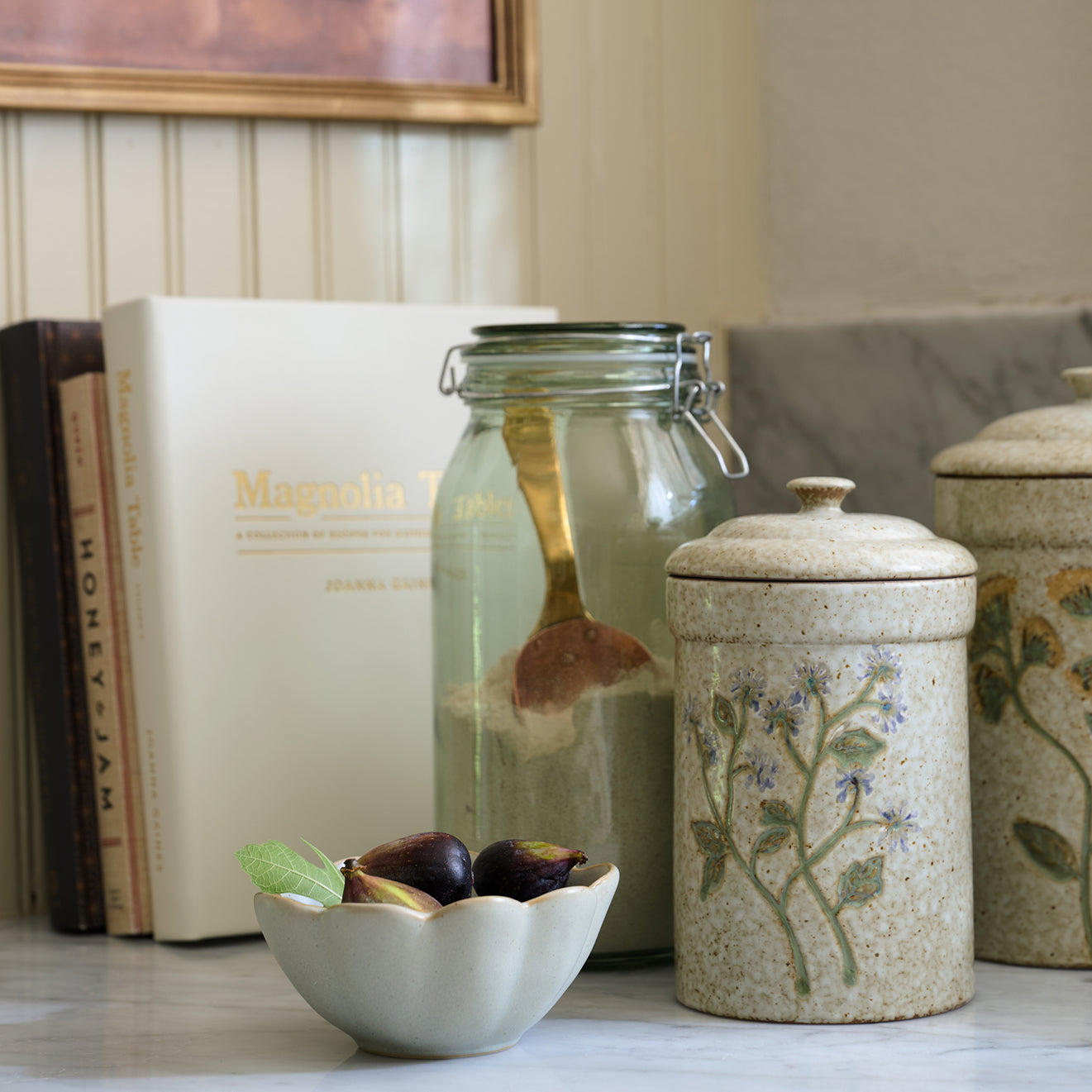 Decorative items including a jar, books, and a bowl with figs on a surface.