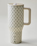 A tall travel mug with a repeating dark gray floral pattern on a warm cream background, featuring a matching cream handle and lid, with the brand name 'HYDRO JUG' printed near the bottom.