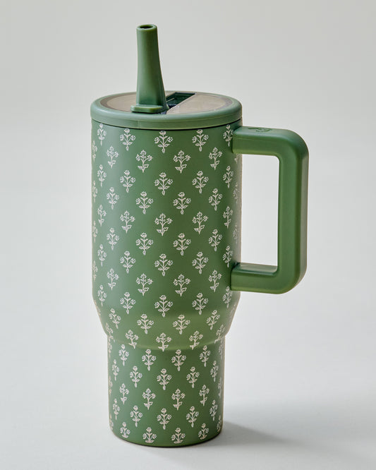 An olive green travel tumbler with a repeating white floral pattern, featuring a matching green handle and straw lid, photographed on a neutral light gray background.