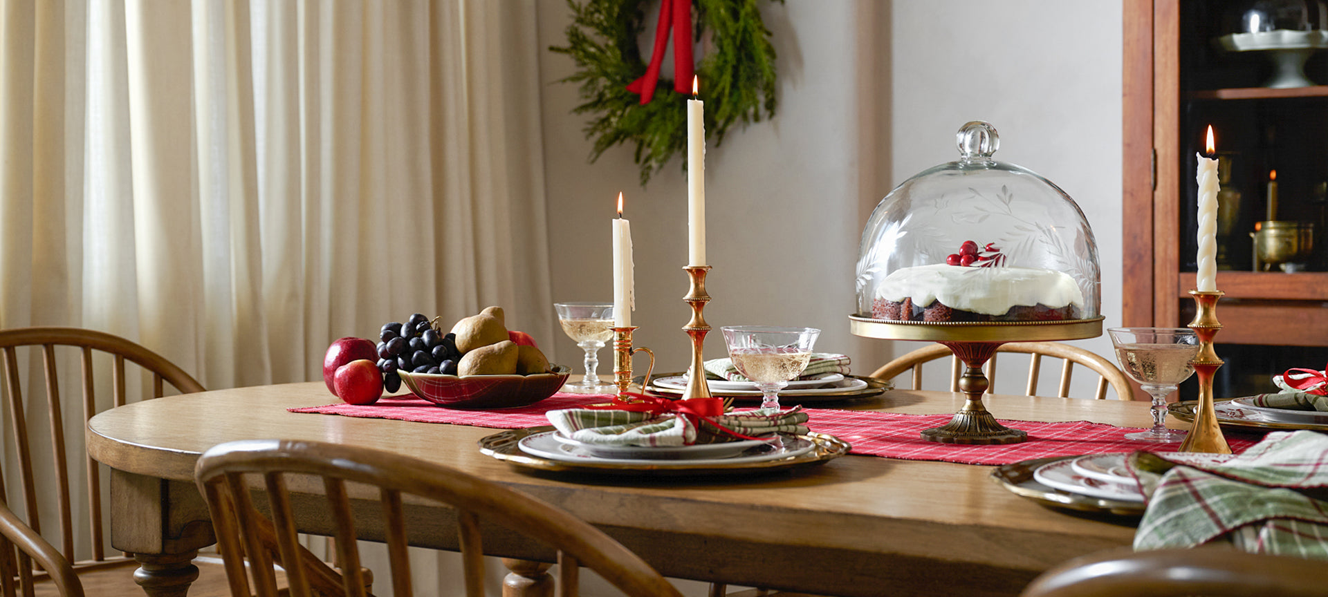 Dining table set for a meal with place settings, candles, and a cake under a glass cloche.