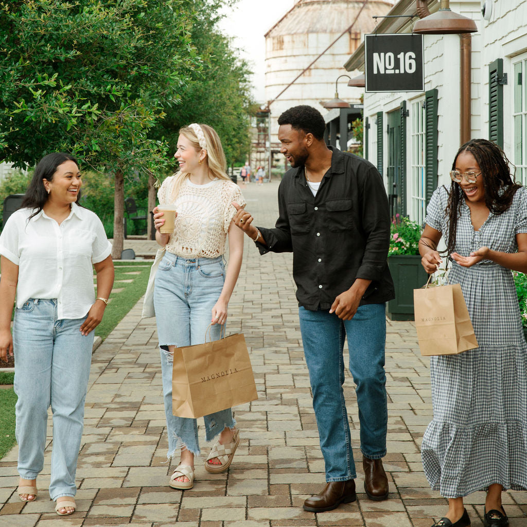Four friends walking together on a sidewalk with shopping bags, smiling and enjoying each other's company.