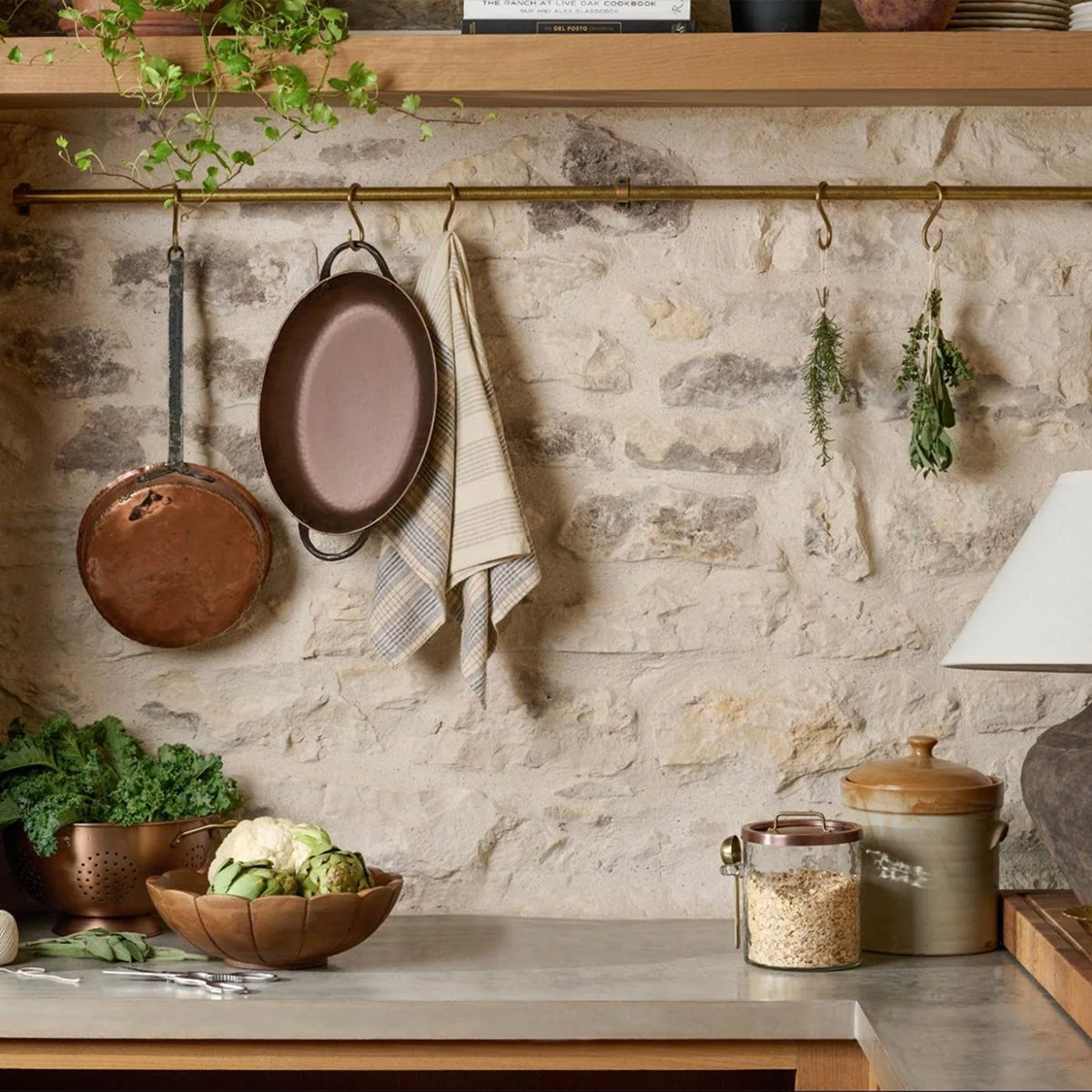 Kitchen with stone wall, hanging pots, and a countertop with vegetables and jars.