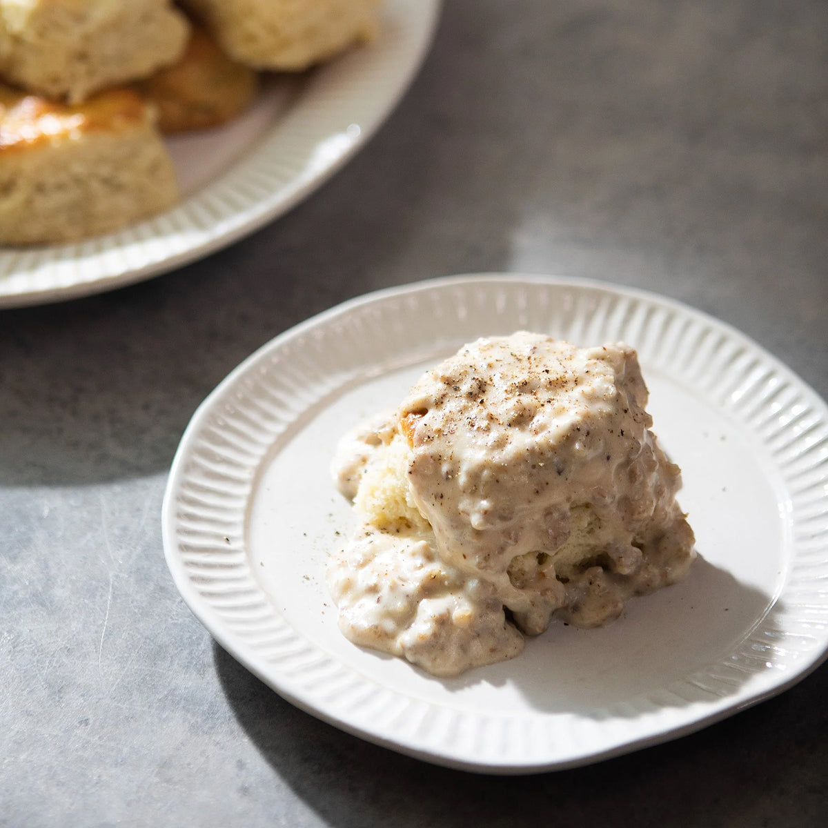 Biscuit with gravy on a white plate on a gray surface.