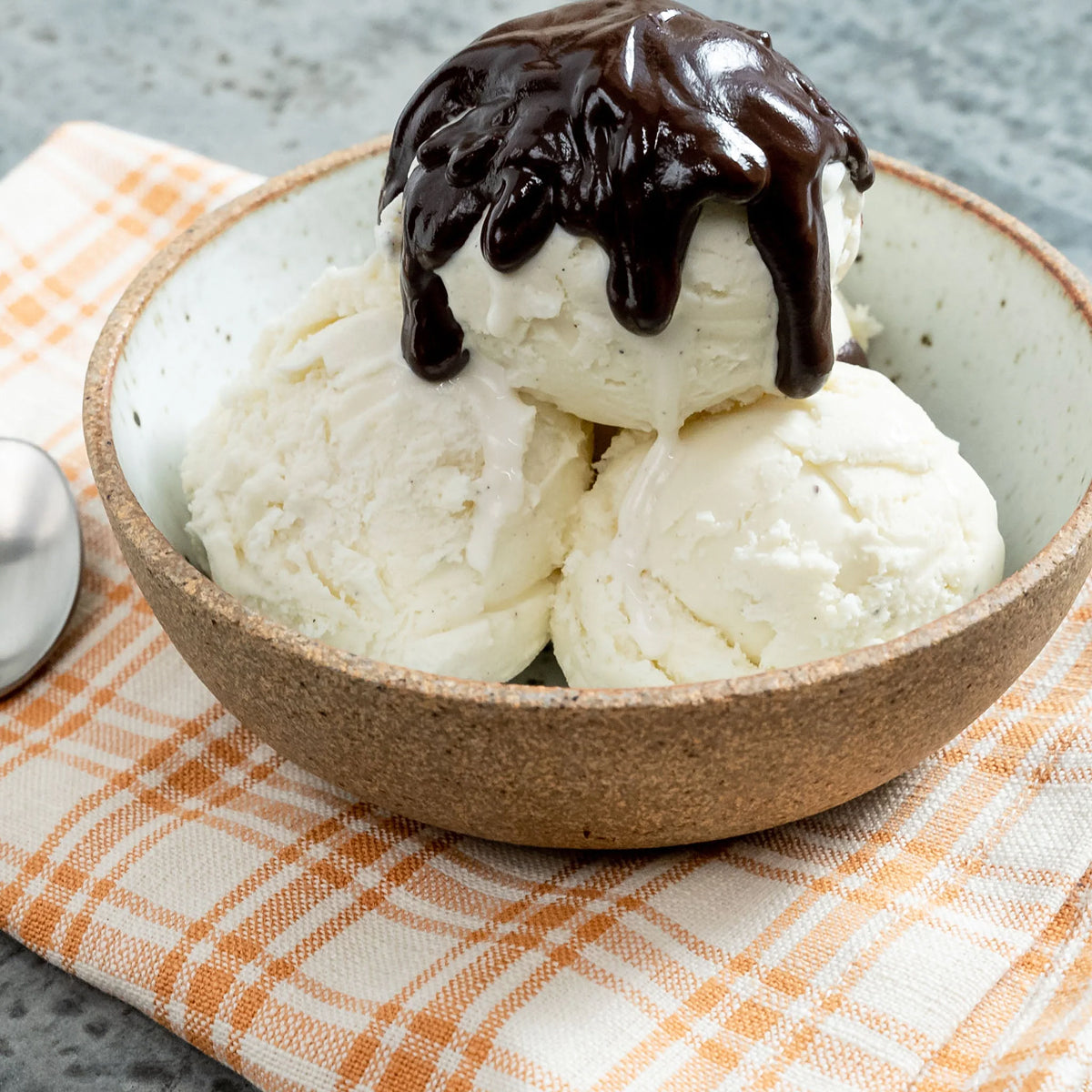 Bowl of homemade ice cream with homemade chocolate sauce on a checkered cloth.