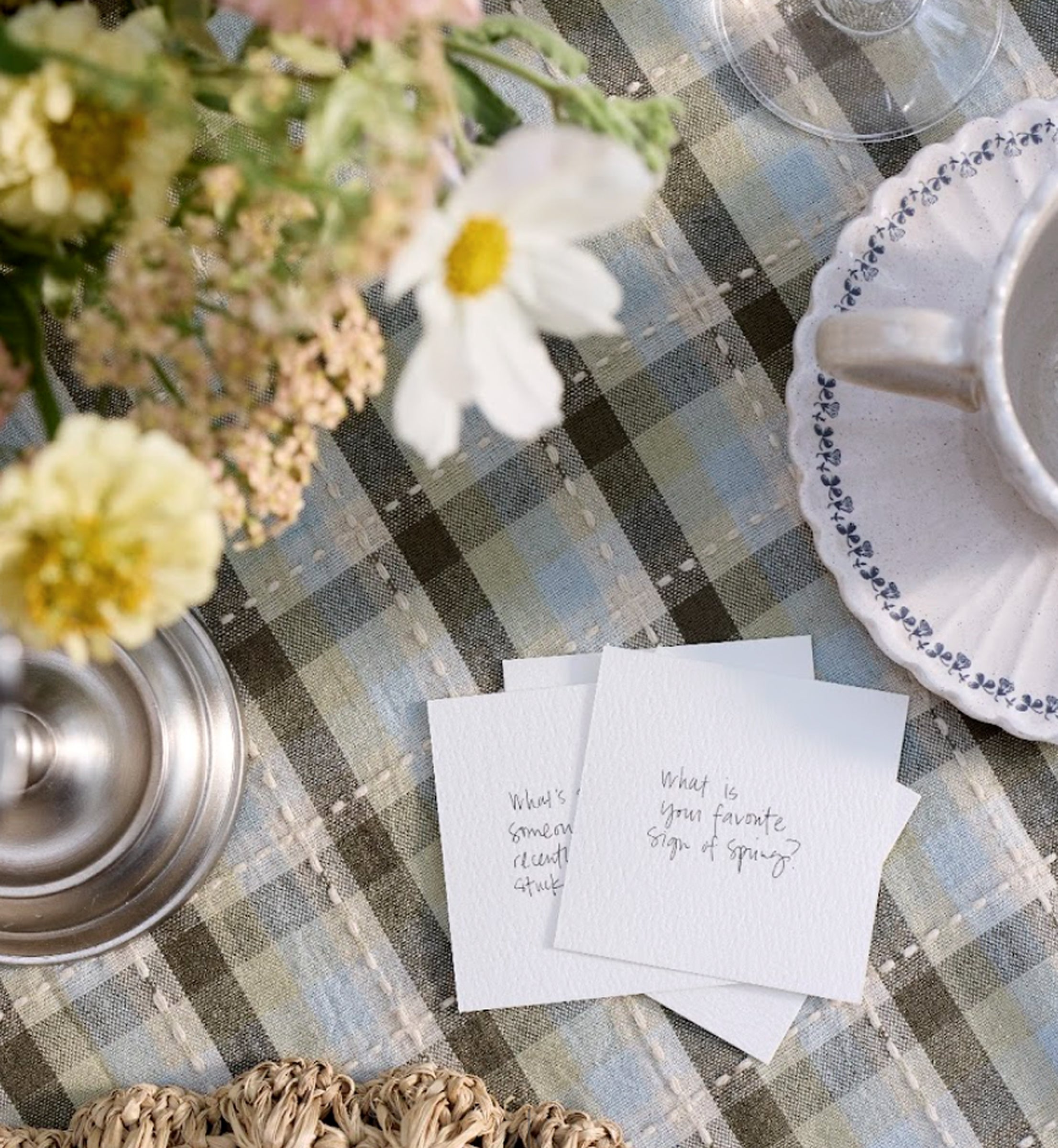 Table setting with flowers, teacup, and question cards on a checkered tablecloth