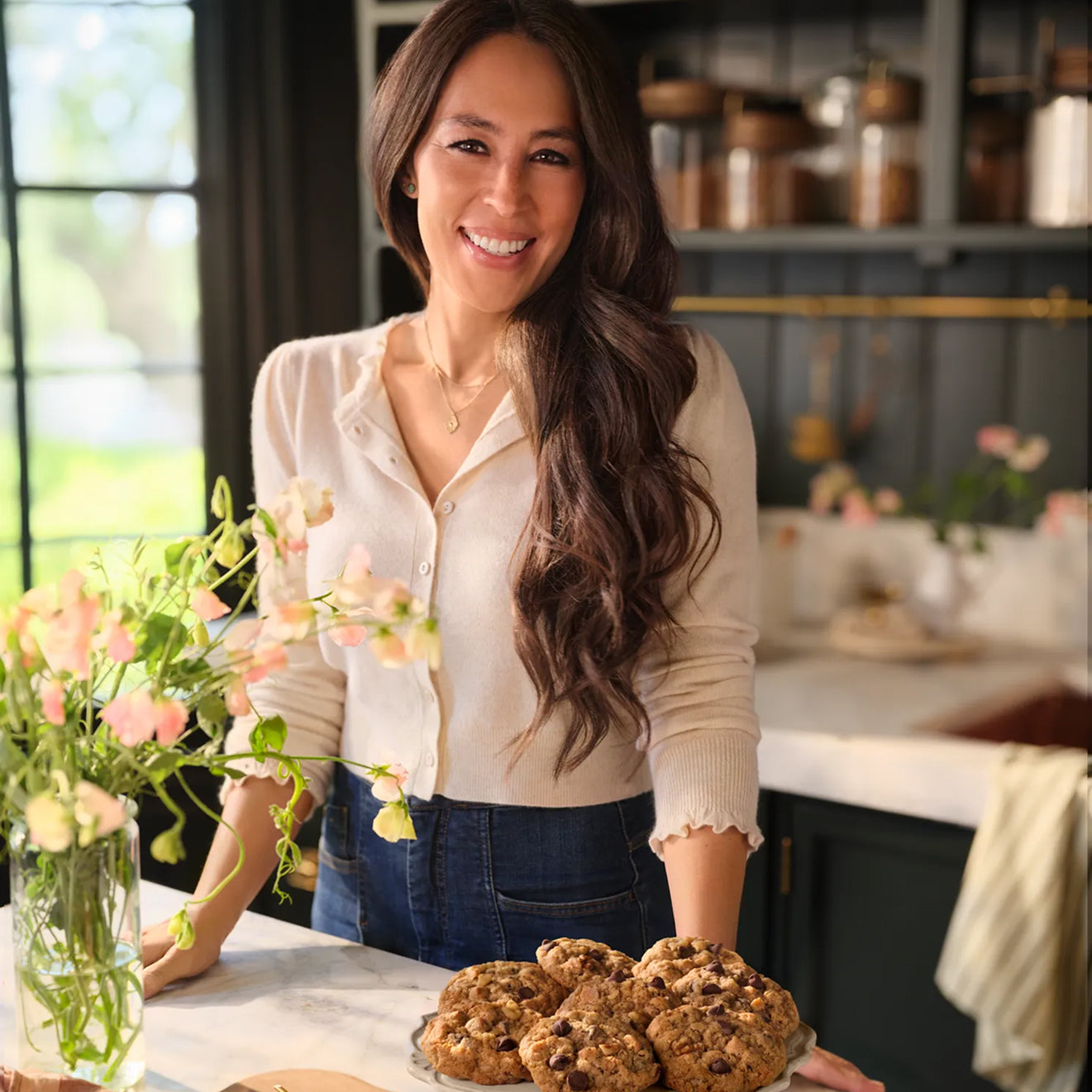 Joanna Gaines standing in her butler's pantry with vase of flowers and a cake plate full of Magnolia Table Silo Cookies.