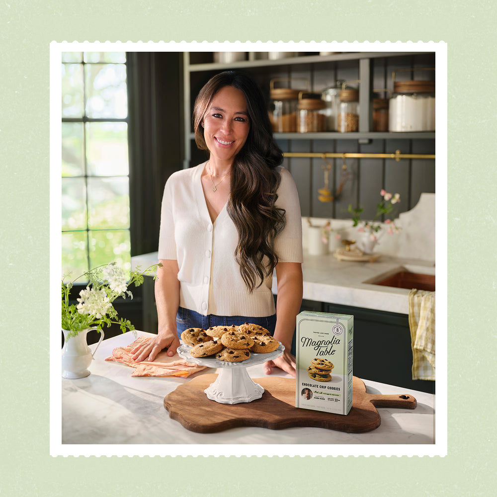Joanna Gaines in her butler's pantry with a plate stand full of chocolate chip cookies and a box of her frozen chocolate chip cookie dough.