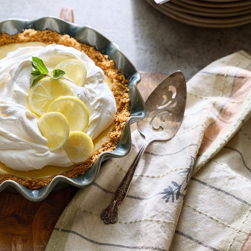 Lemon pie with whipped cream and lemon slices on a metal pie dish with a serving spatula.