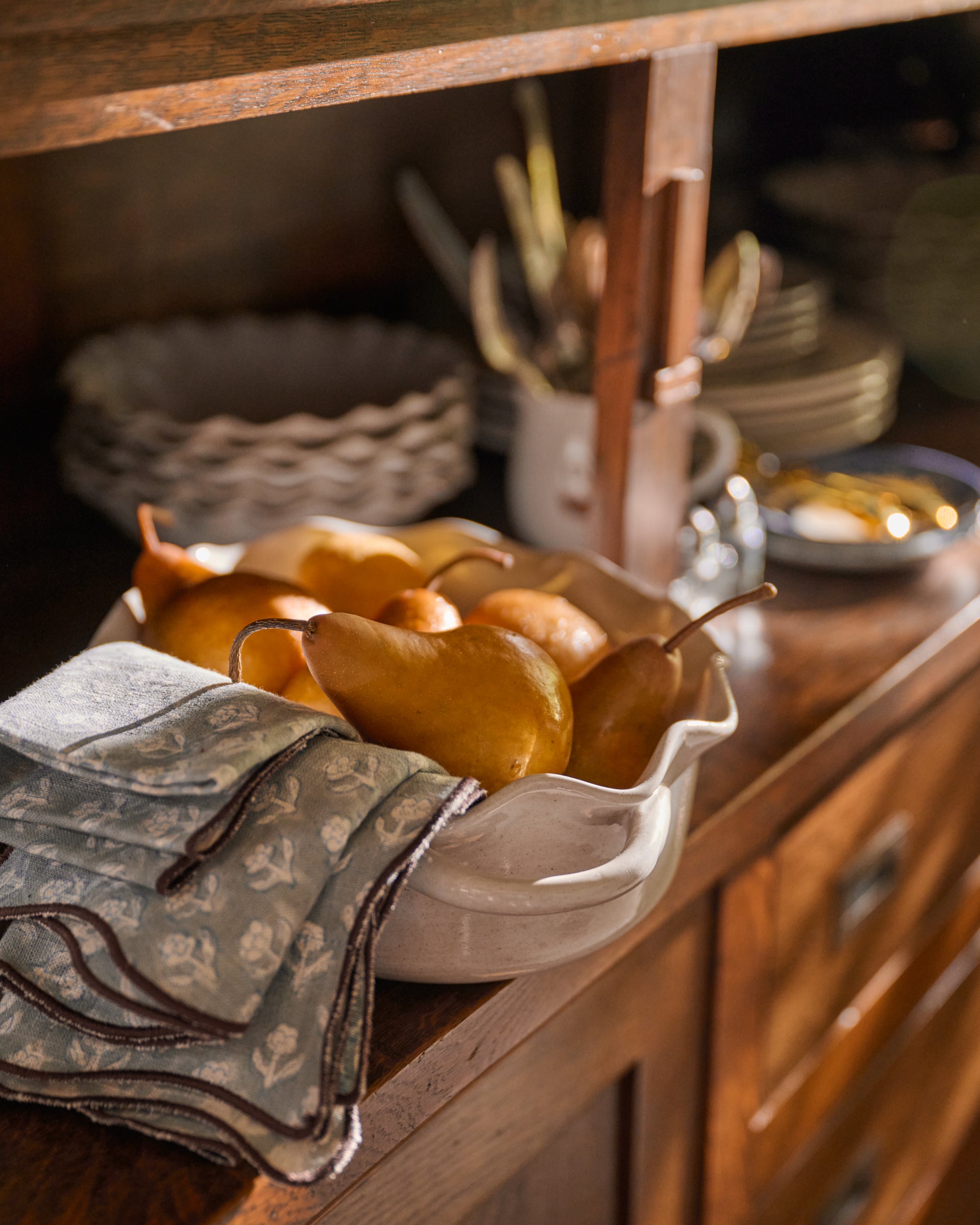 A white ceramic baking dish filled with golden-brown pears, set on a rustic wooden cabinet next to a folded patterned cloth napkin.