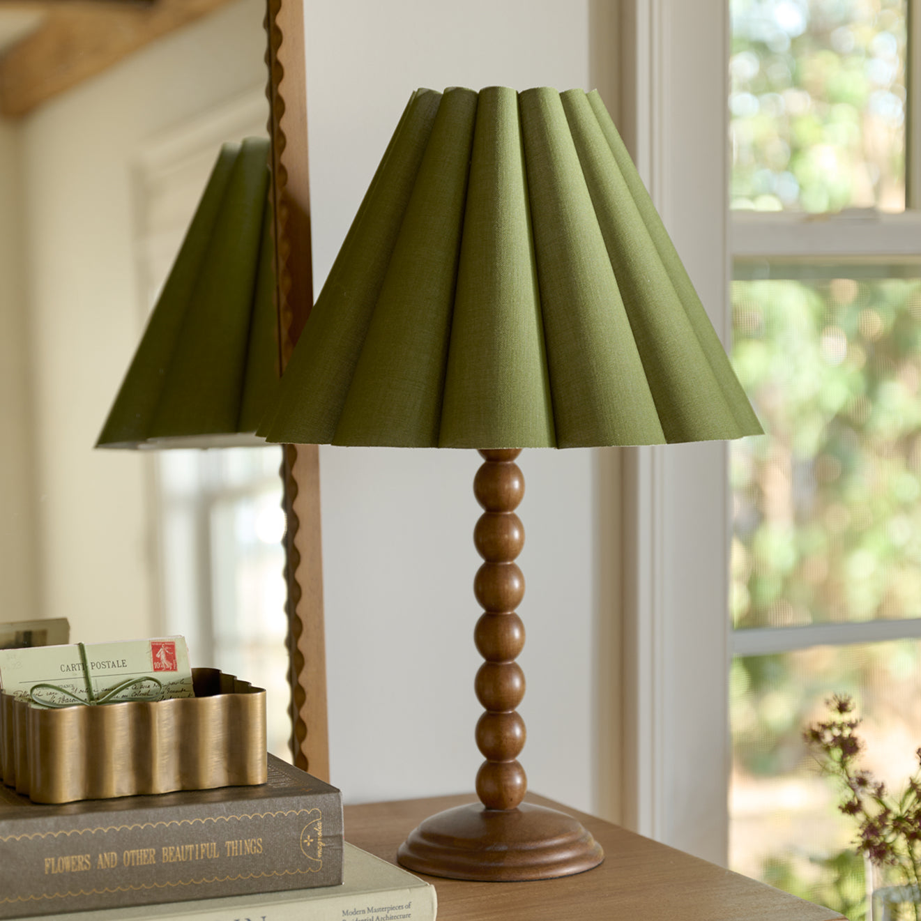 Green lamp with wooden base on a shelf in a room with a window