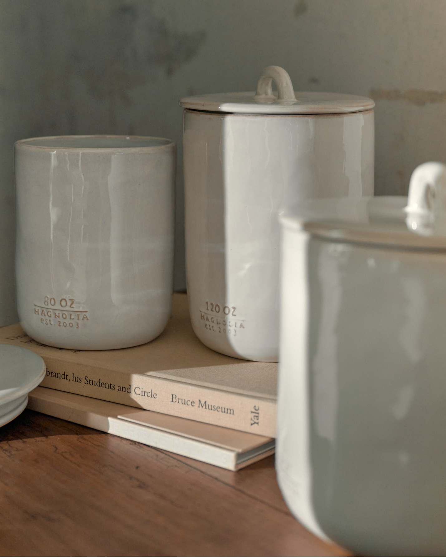 Set of three Mia cream glazed canisters in different sizes sitting on top of a couple stacked books.