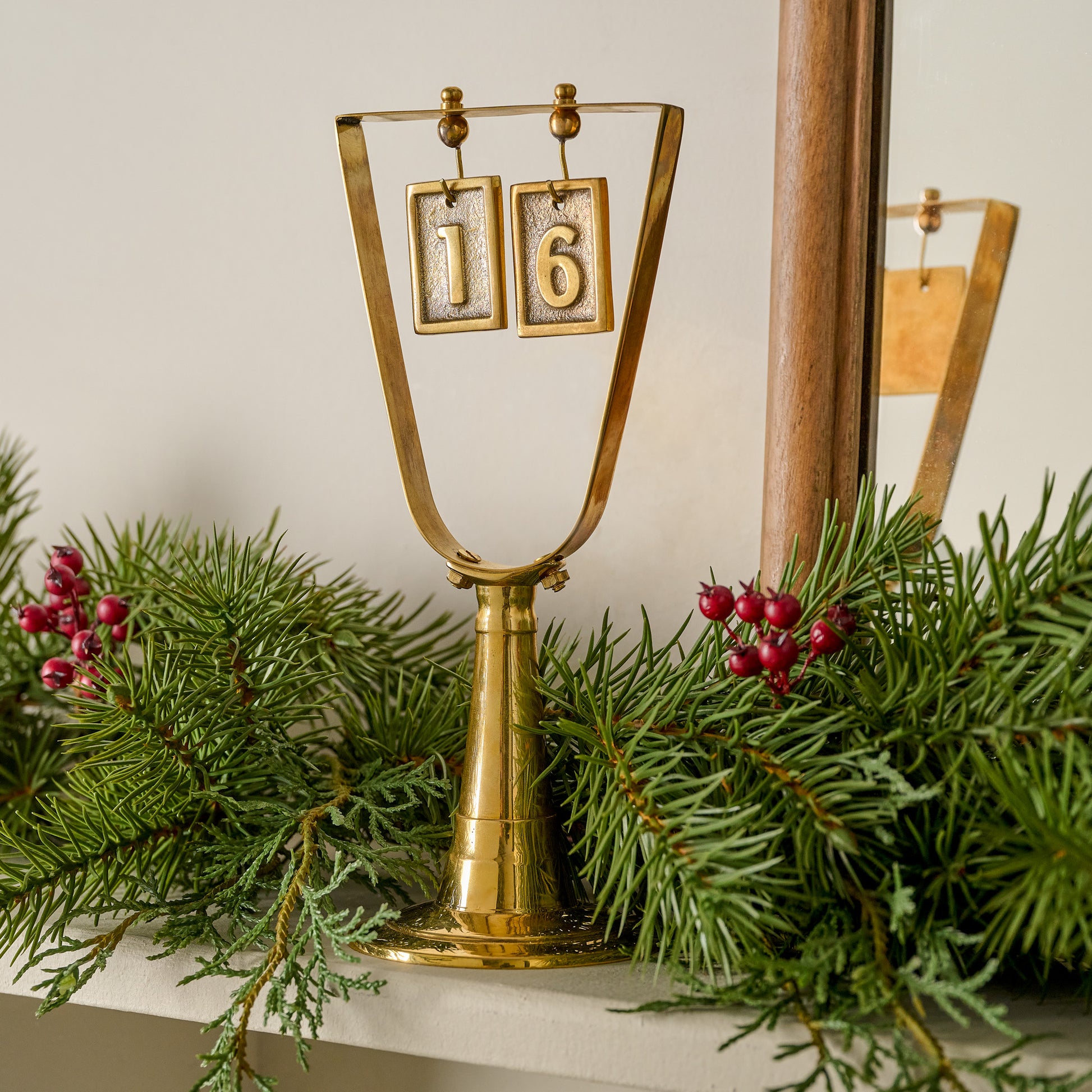 Solid Brass Countdown to Christmas shown on mantel with greenery