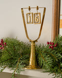 Solid Brass Countdown to Christmas shown on mantel with greenery
