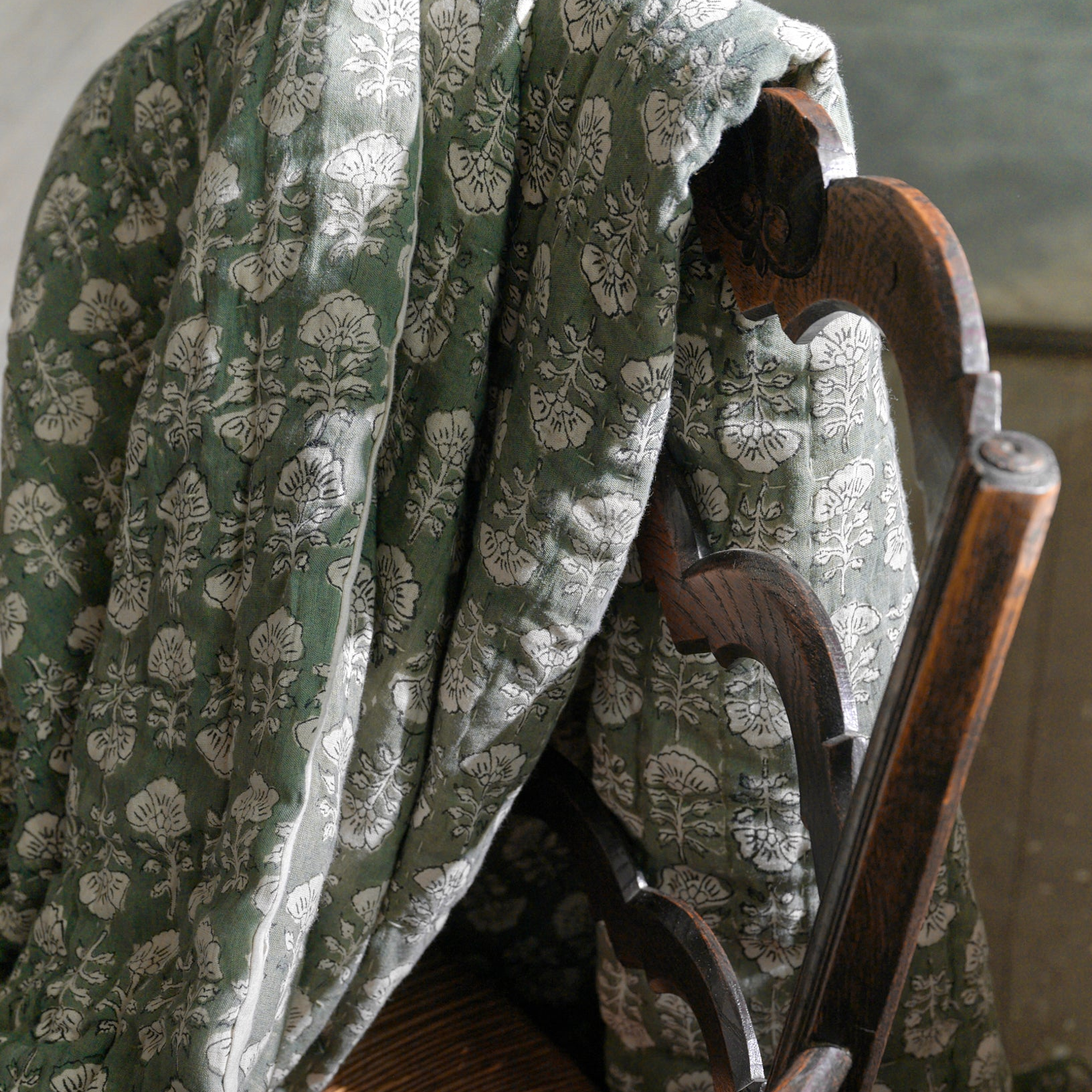 Flora green bedding laying over an old wooden dining chair.