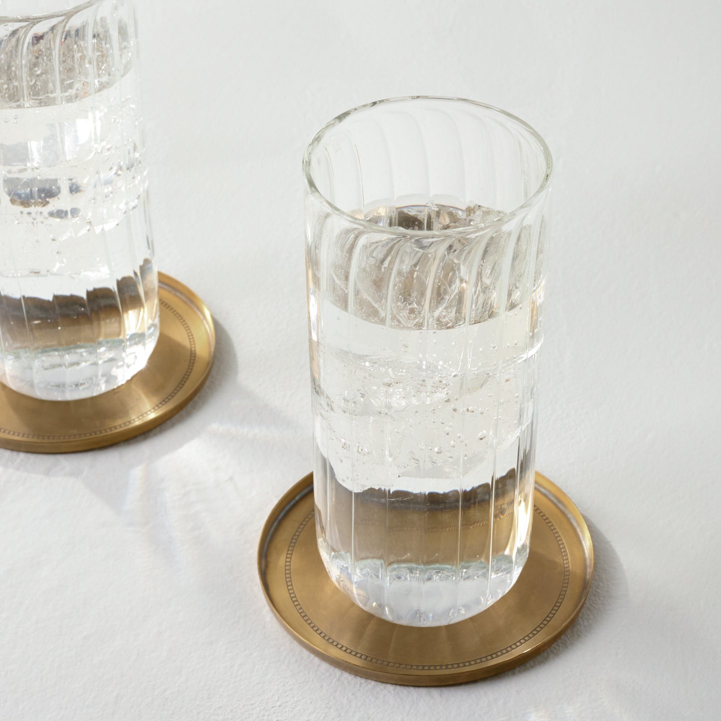 Magnolia Etched Brass Coaster Set of Four shown with tumbler glass