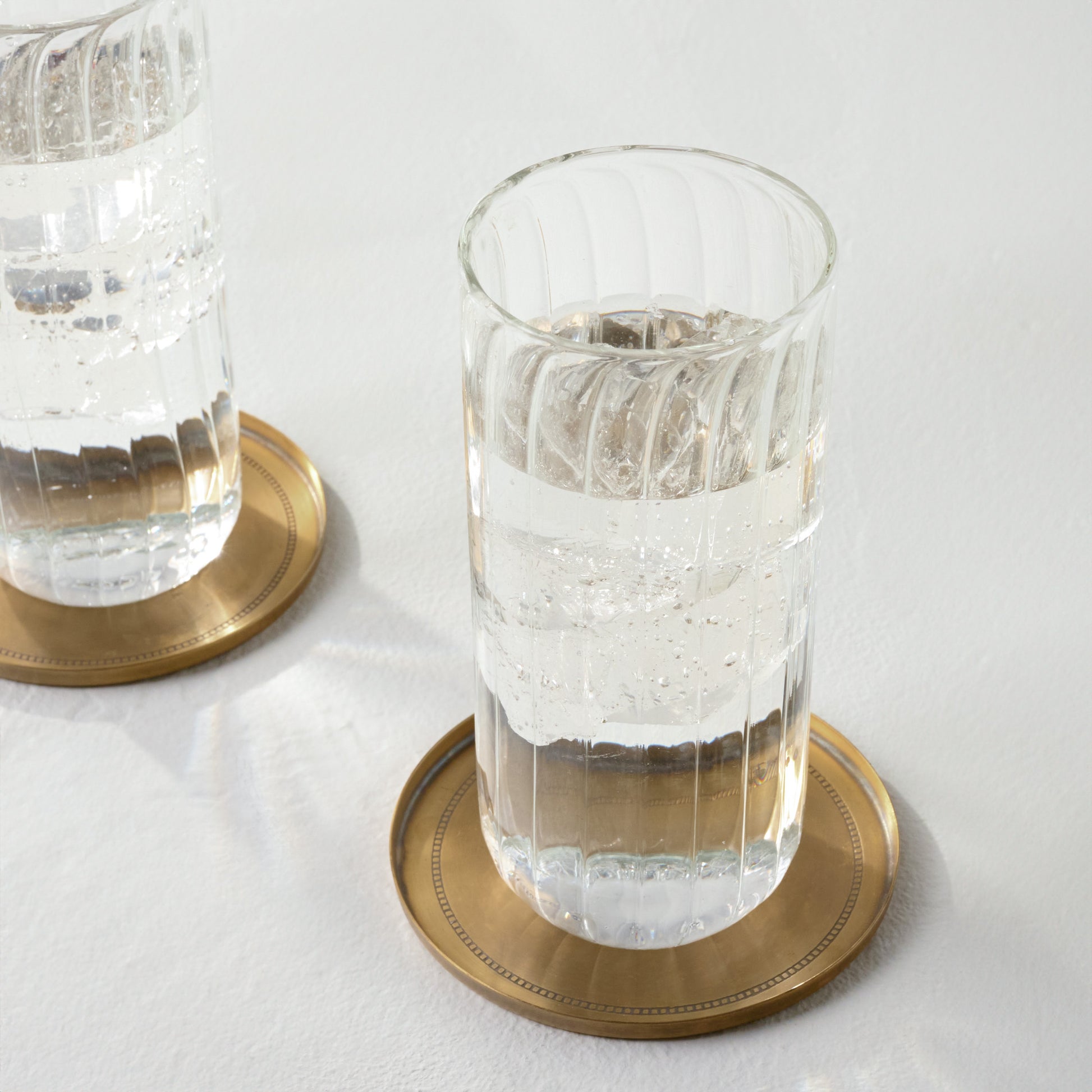 Magnolia Etched Brass Coaster Set of Four shown with tumbler glass