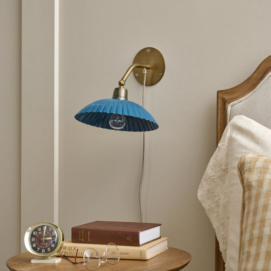 Chester Enamel Plug-in Sconce - Blue with Brass shown on wall next to bed