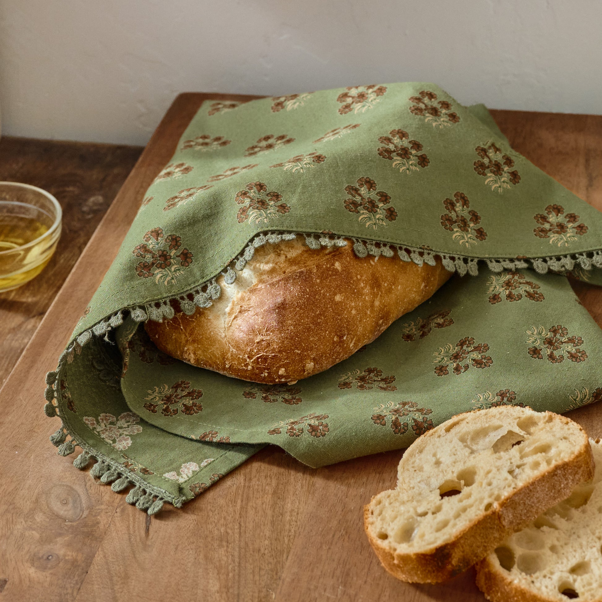 Magnolia Olive Green Block Printed Tea Towel shown wrapping bread