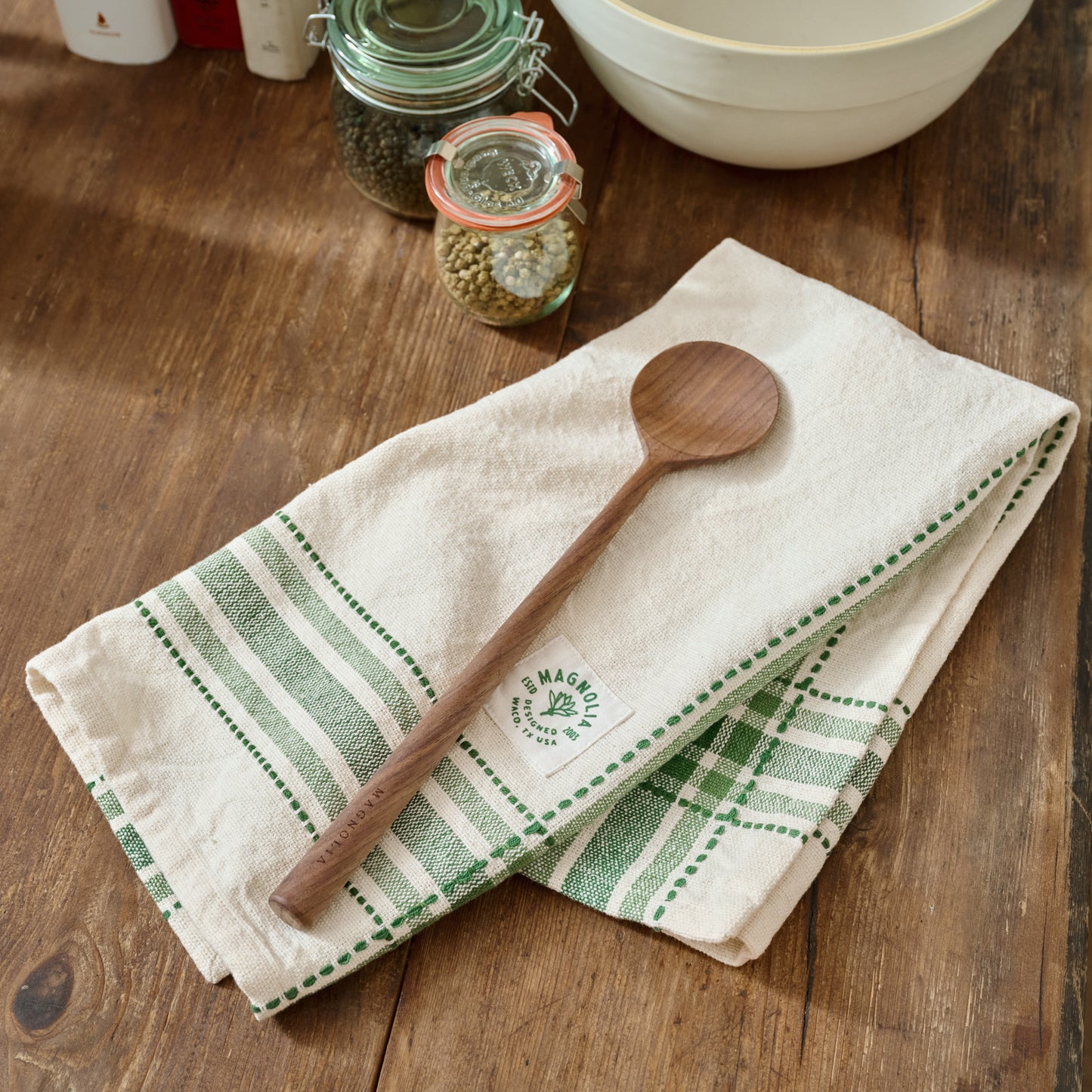 Magnolia Vintage Green Border Tea Towel shown on table with wooden spoon