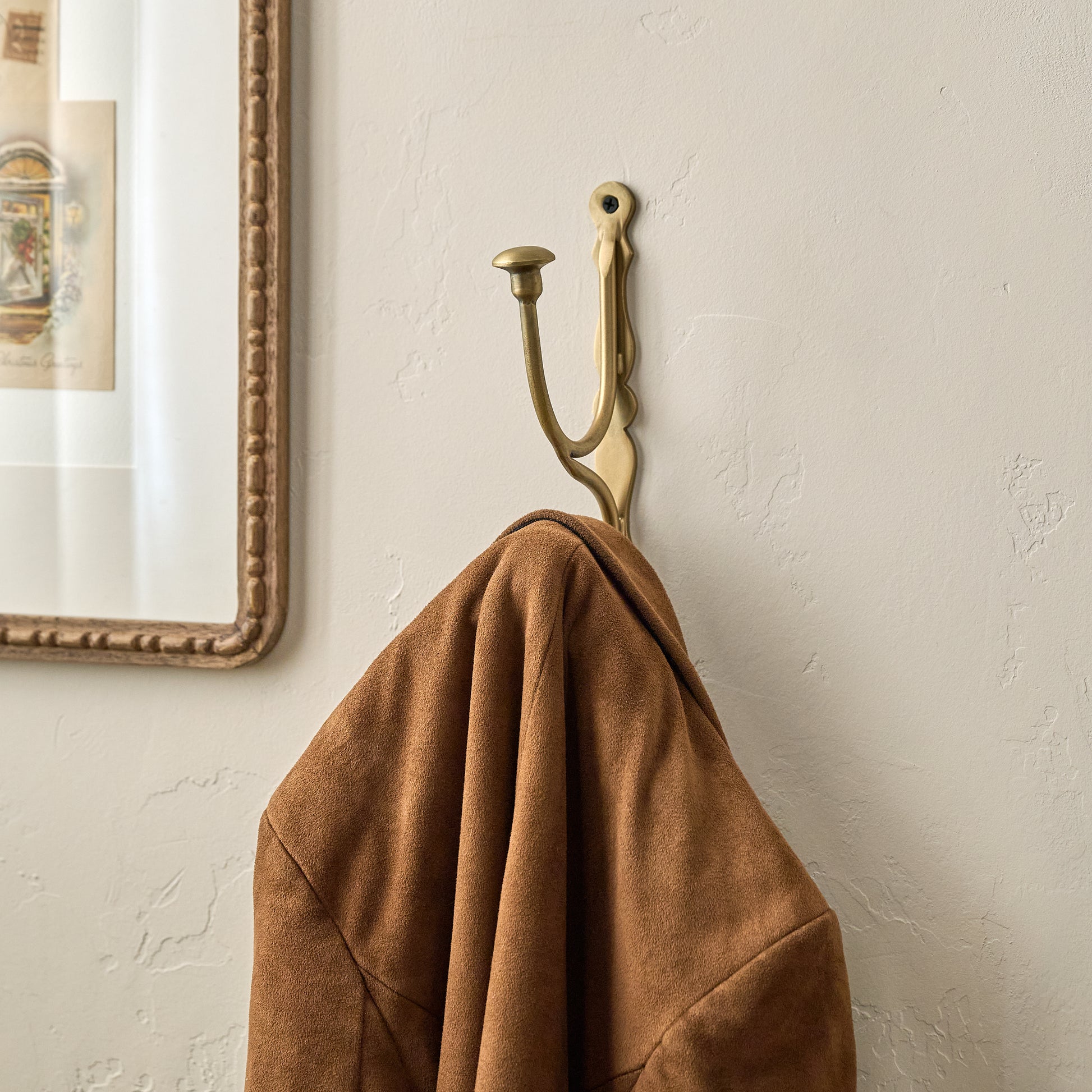 Mia Antiqued Brass Wall Hook shown with jacket hung on it