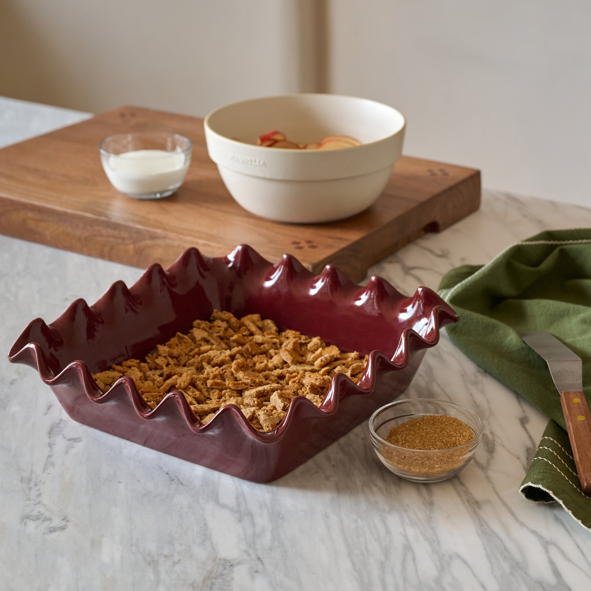 Syrah Scalloped 9x9 Baking Pan shown with food on kitchen counter