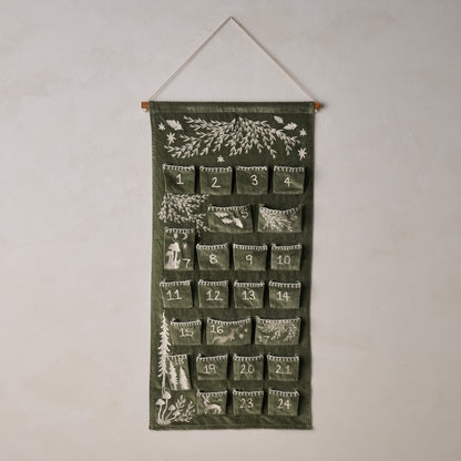 Green advent calendar with nature-themed designs hanging on a white wall.