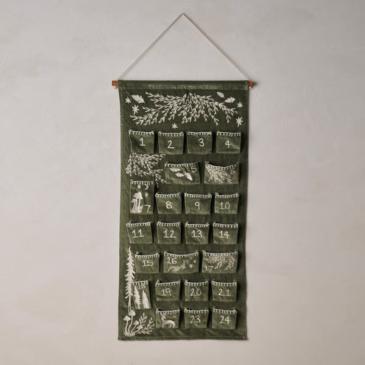 Green advent calendar with nature-themed designs hanging on a white wall.