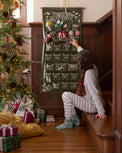 Child interacting with a Christmas advent calendar next to a decorated tree.