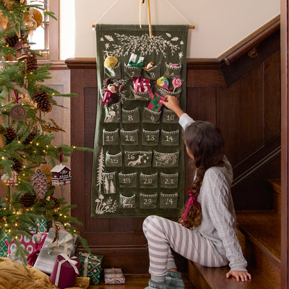 Child interacting with a Christmas advent calendar next to a decorated tree.