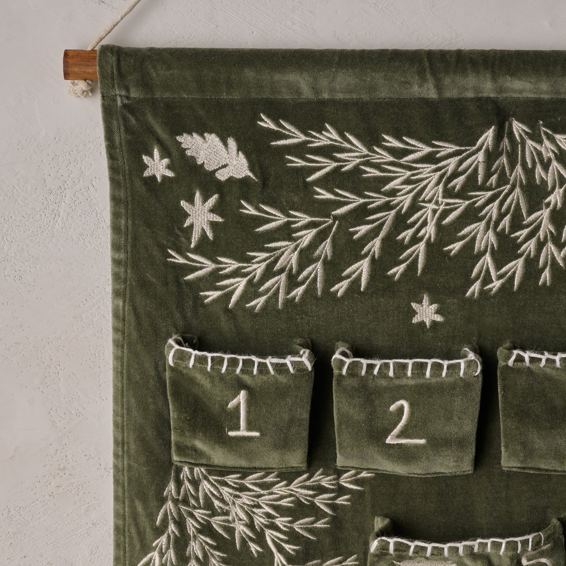Green fabric wall hanging with embroidered designs and numbers on a white wall.