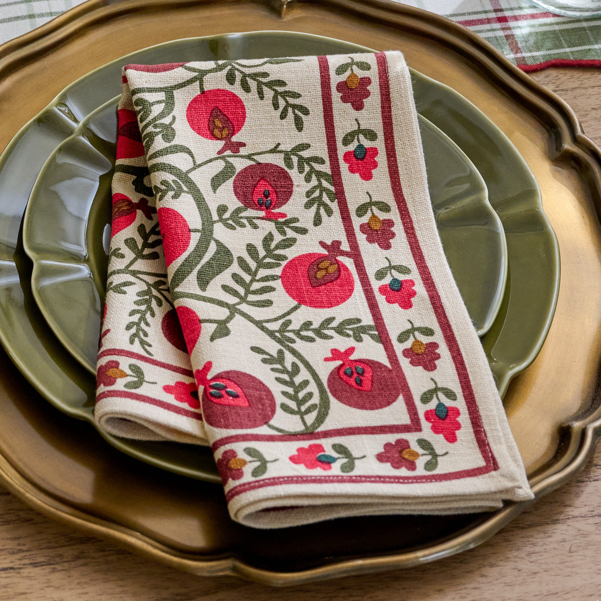 Festive Pomegranate Napkin shown folded and set on holiday place setting