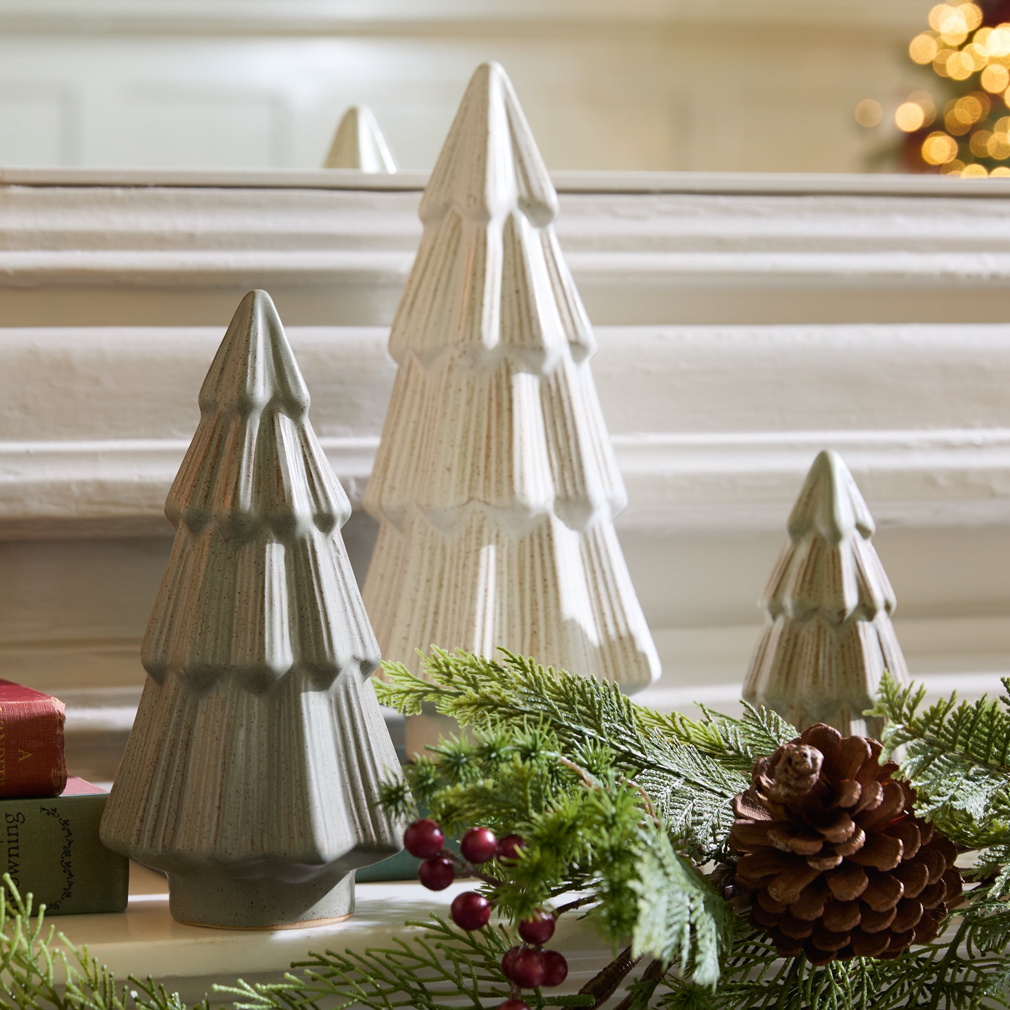 Decorative ceramic Christmas trees with greenery and pinecones on a windowsill.
