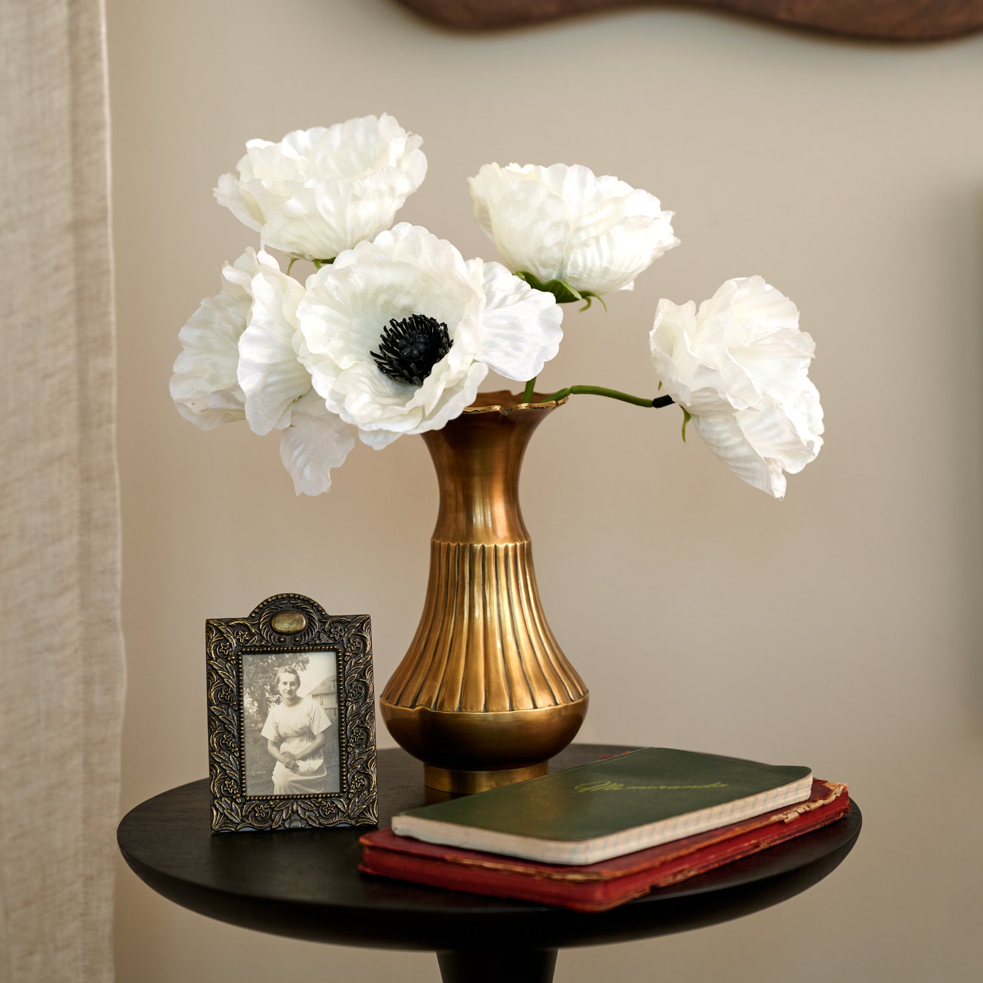 Anna Antiqued Solid Brass Vase (small) with white flowers next to picture frame on top of end table