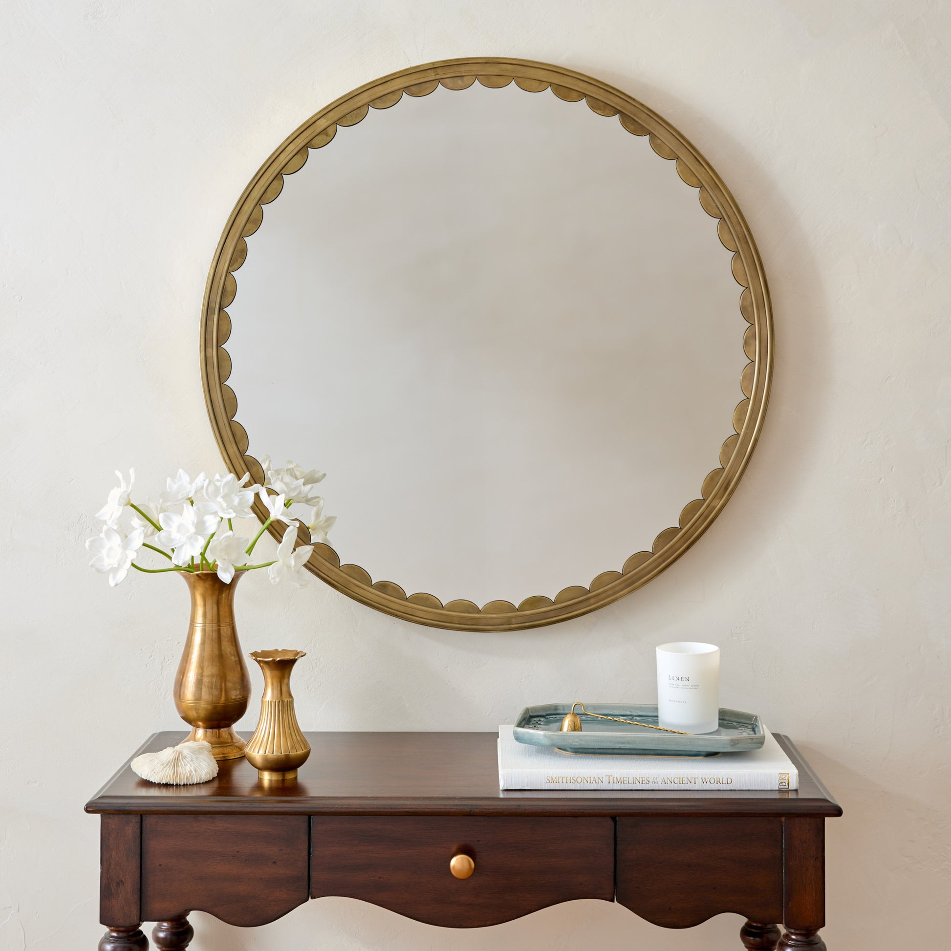 Julie Round Brass Scalloped Mirror in a room with brass vase with white daffodils and home fragrance