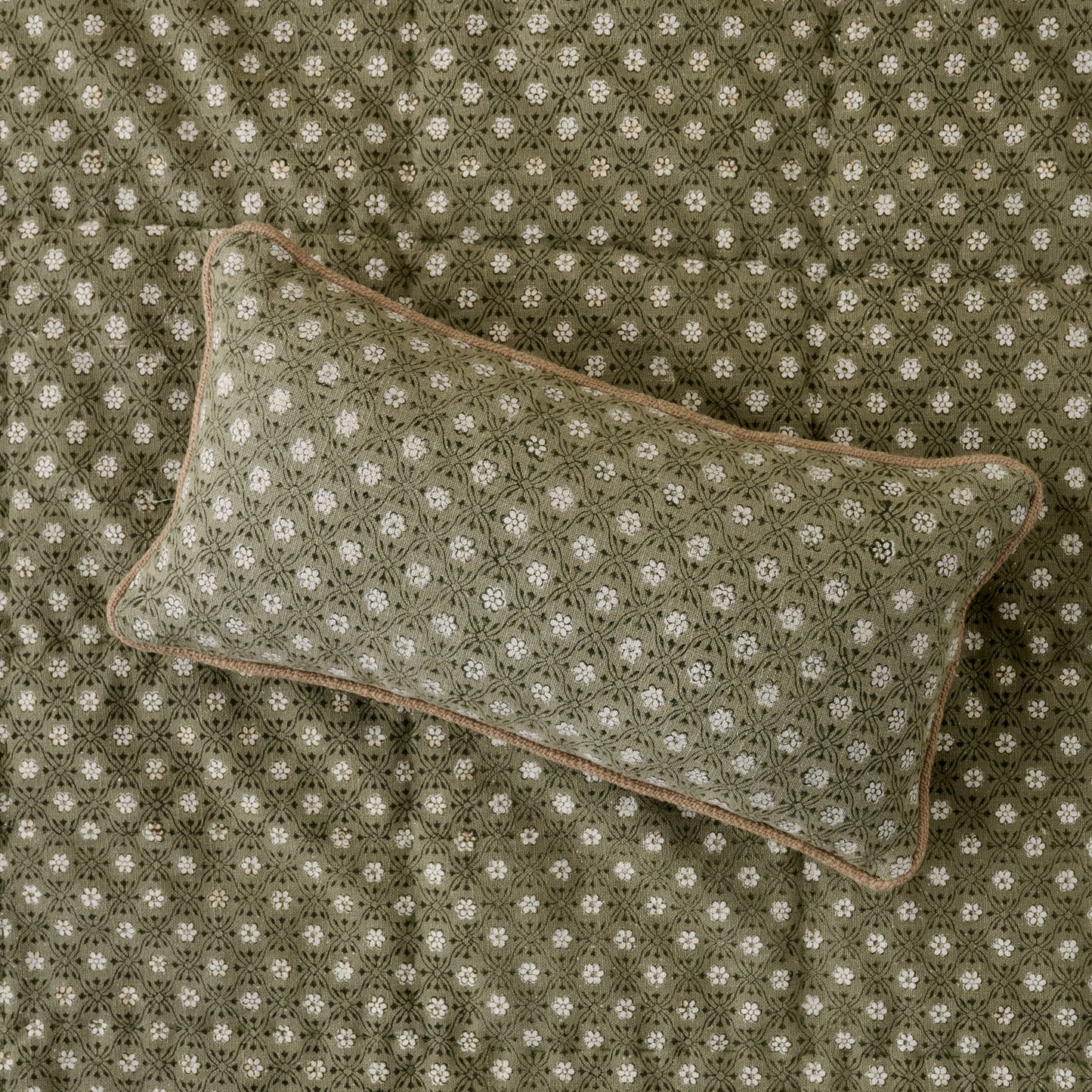 Thea Reversible Lumbar Pillow (small) on top of quilt bedding