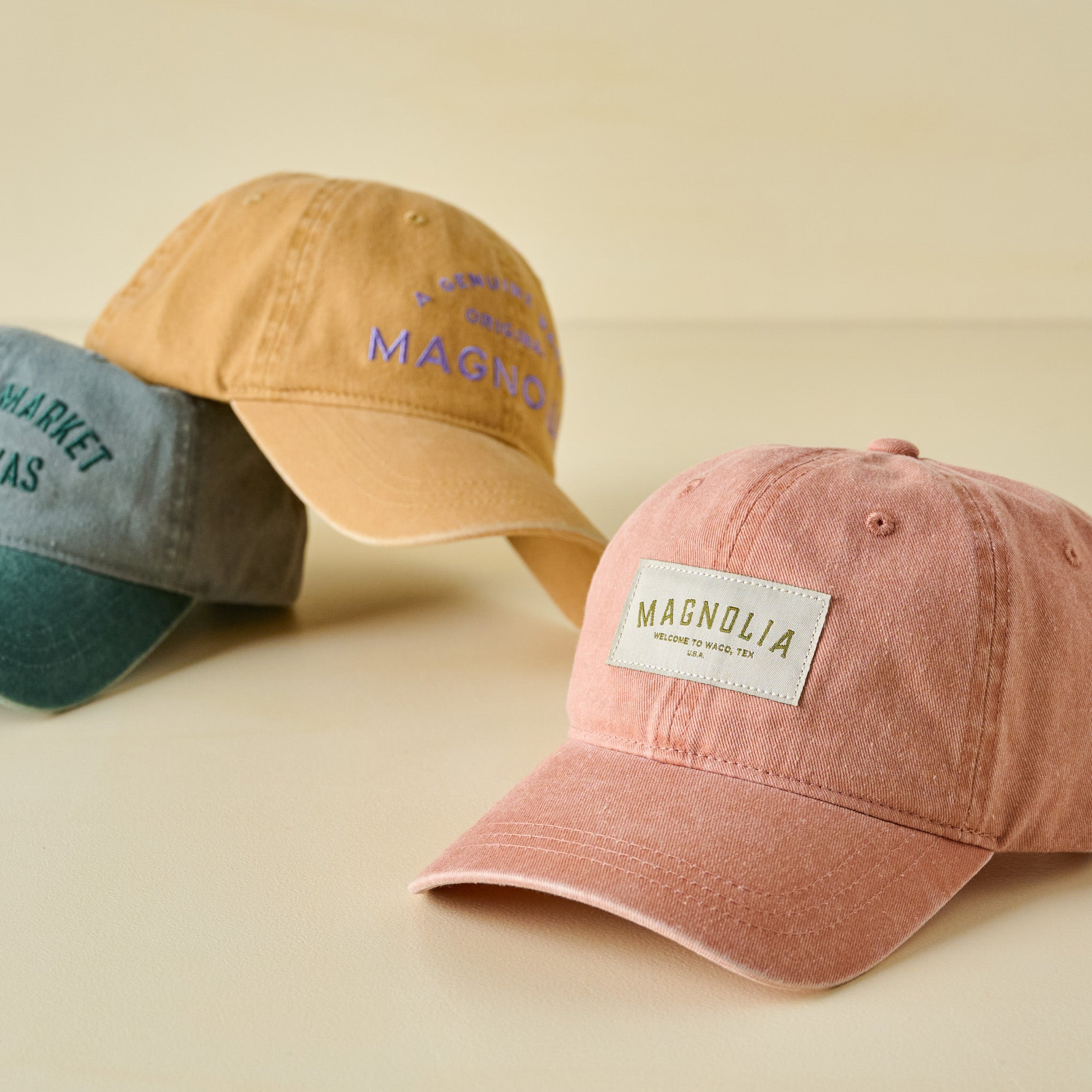 Three baseball caps with 'Magnolia' branding on a beige background