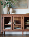 Wooden sideboard with glass doors displaying decorative items, vases, and a plant.
